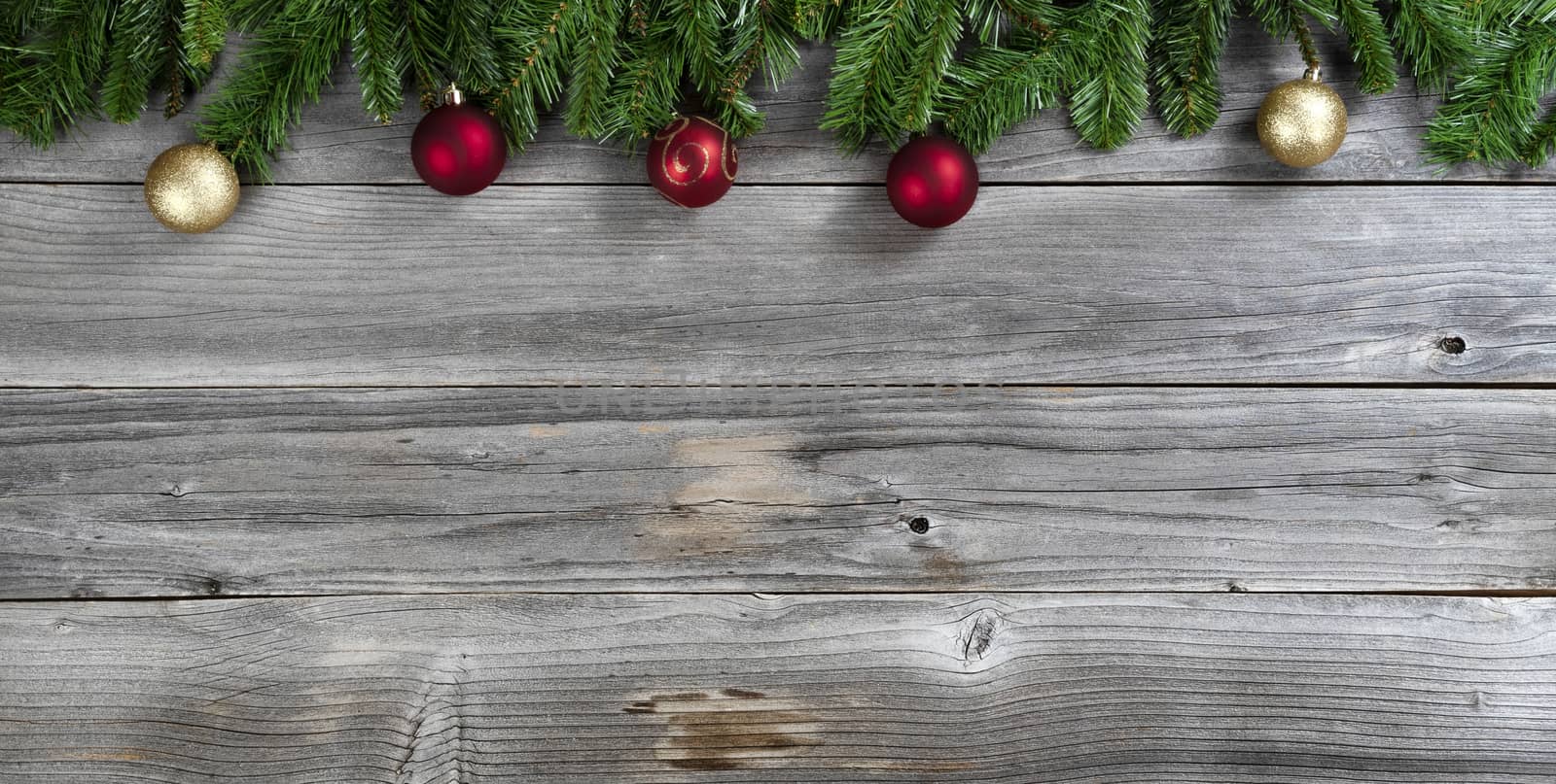 Merry Christmas and Happy New Year with red ball ornaments inside of fir branches on rustic wooden boards 