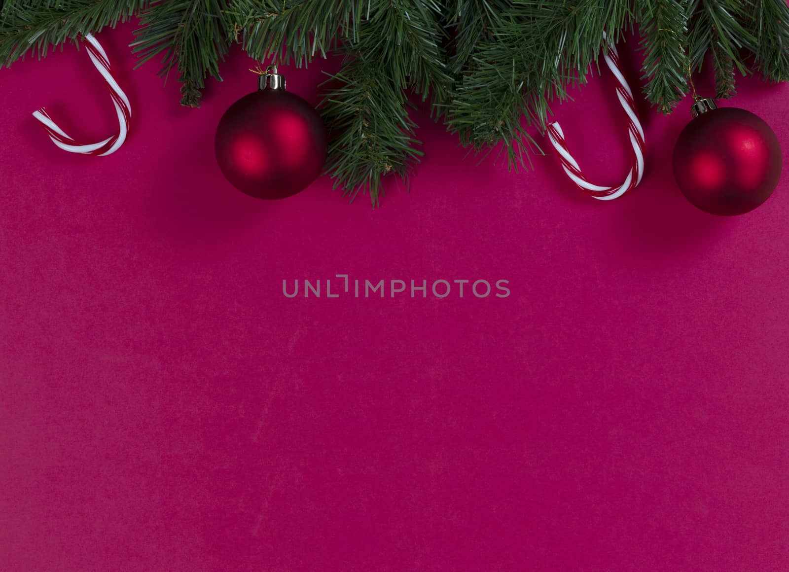 Merry Christmas and happy New Year on a red background with evergreen branches plus ball ornaments and candy canes 
