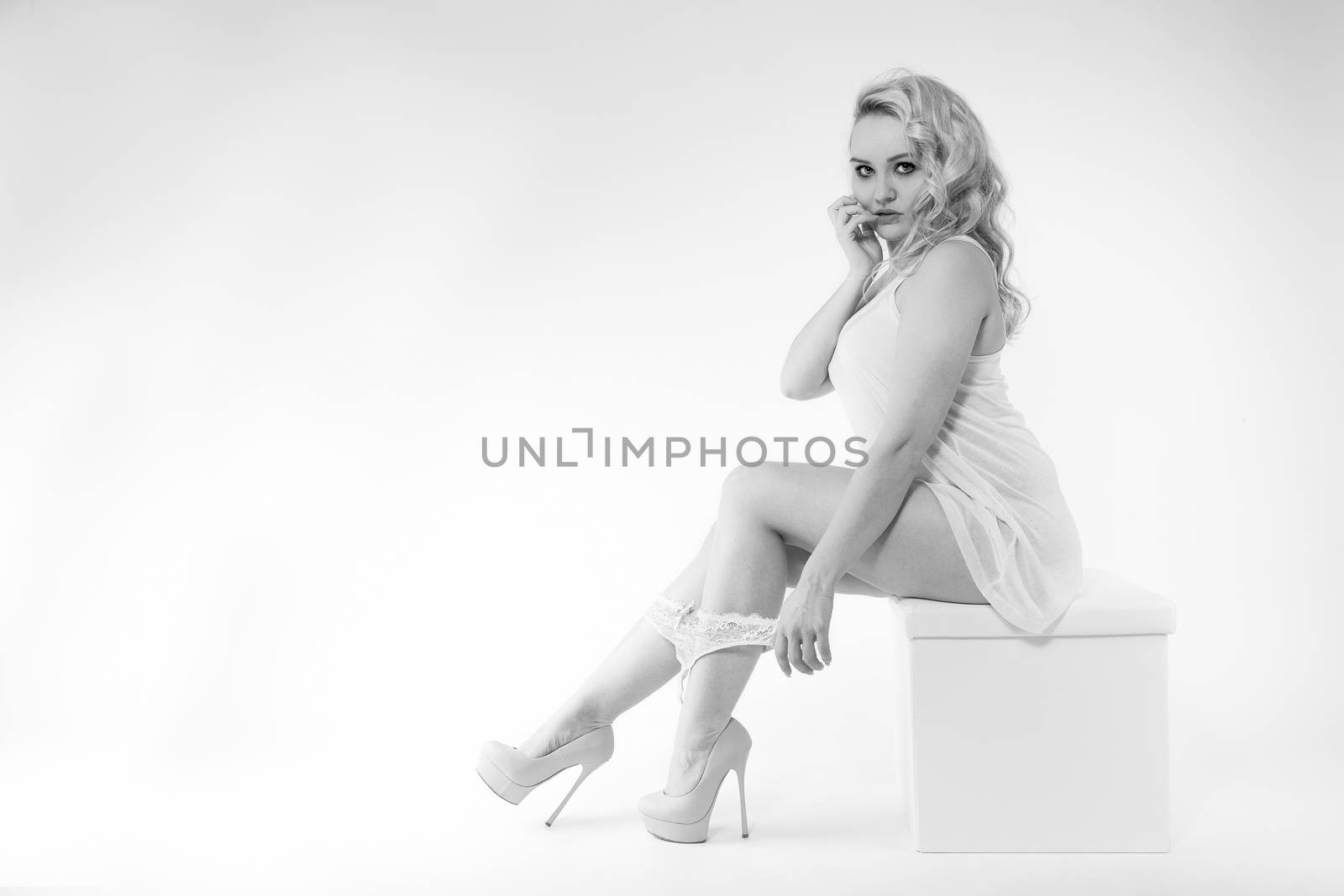 Young woman sitting on a stool in white top, high-heels and lingerie