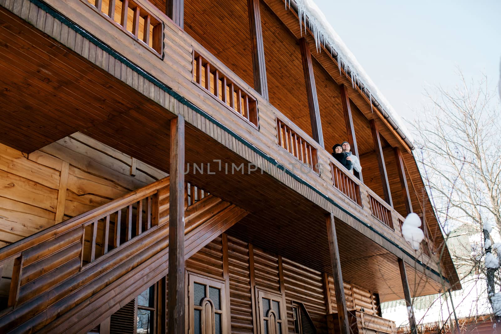 couple of young people a guy and a girl on the porch of a snow-covered wooden house in the winter mountains