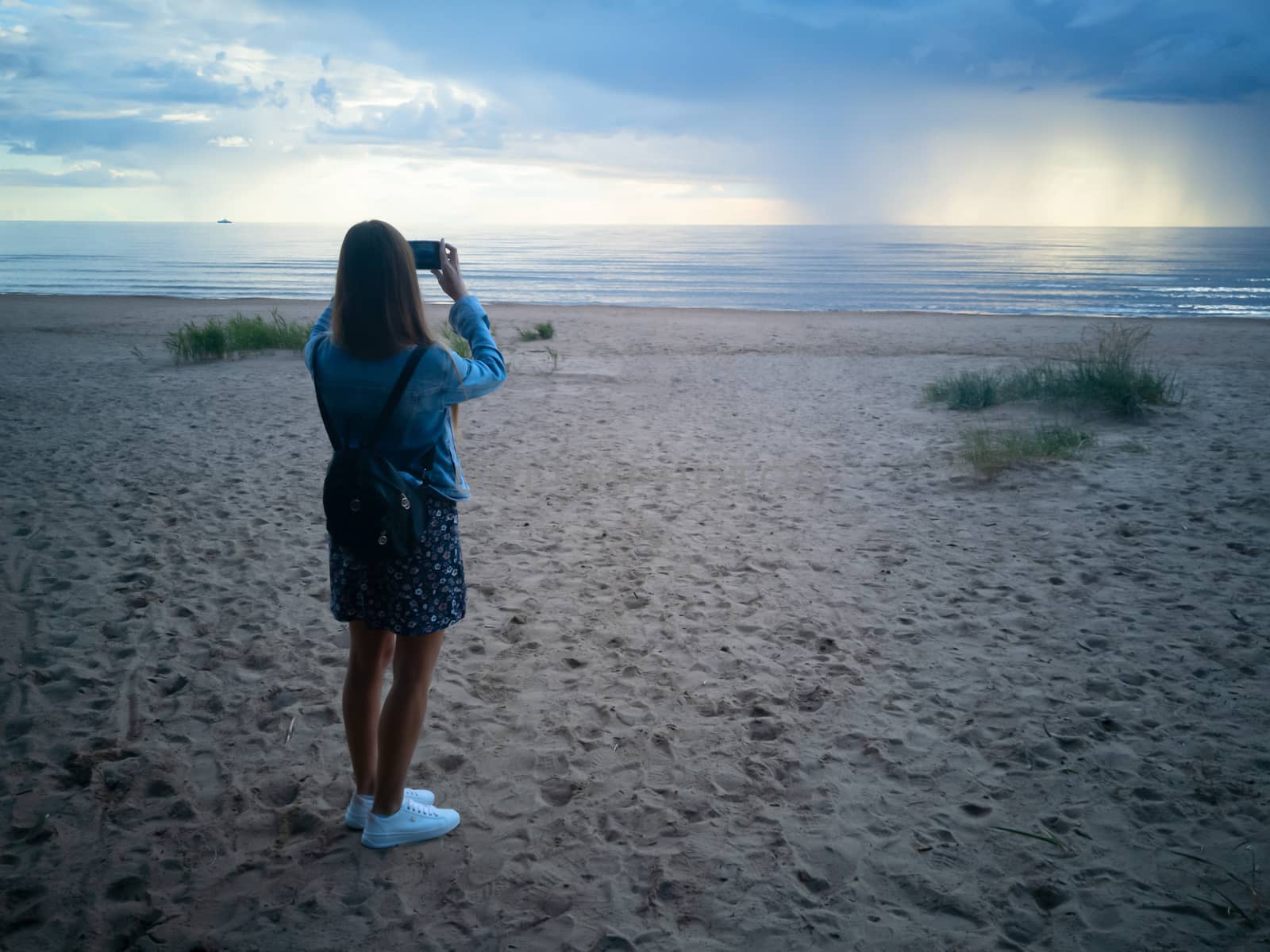 beautiful alone girl on the beach. Girl looking at stormy sea and taking a picture with smarphone. The spectacular Storm with rain Is Coming in Estonia. Baltic sea