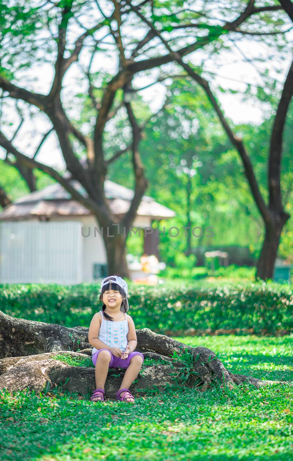 happy little girl wear hat sitting on tree root in the park