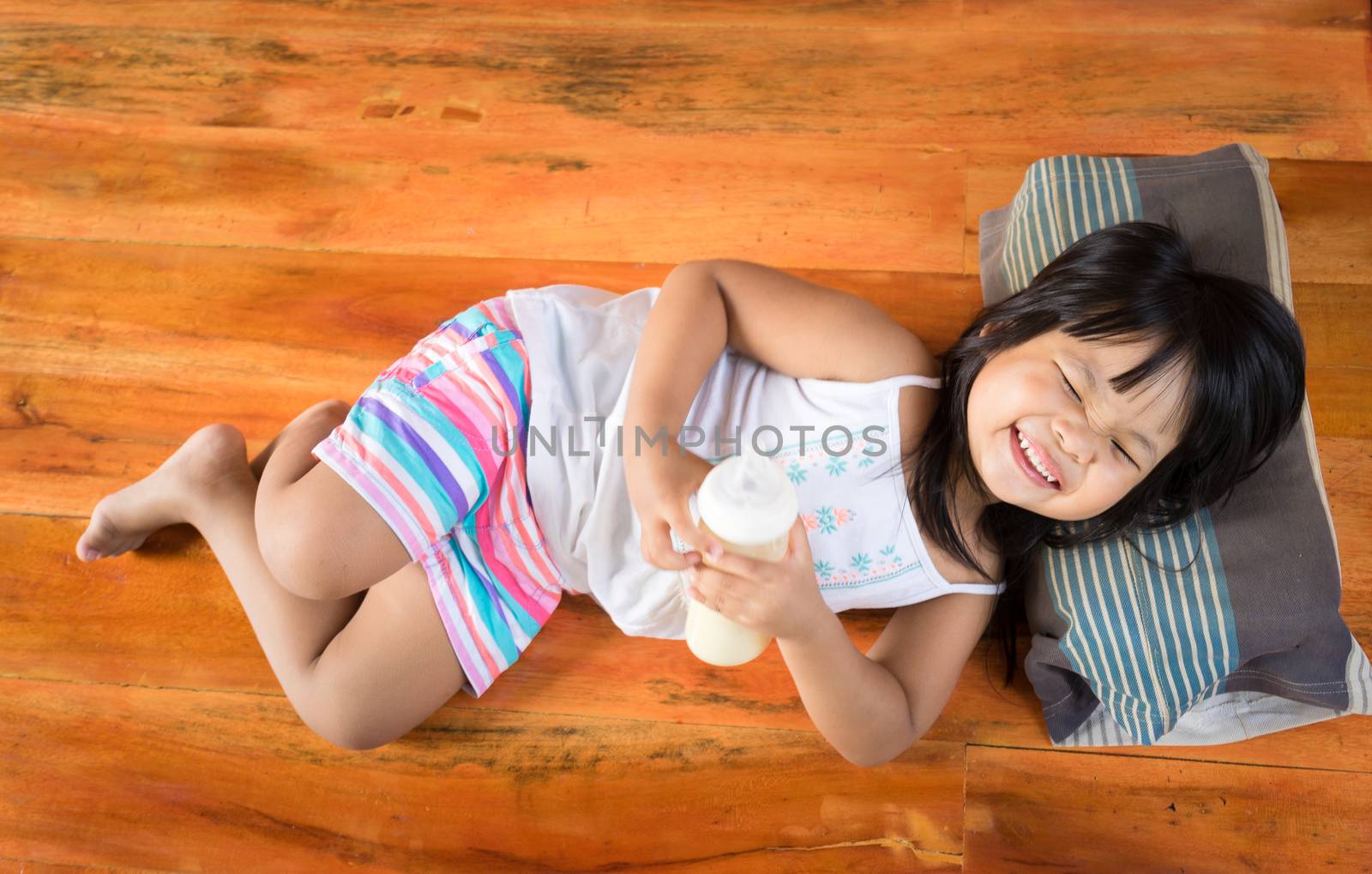 little girl lie leisurely while holding a bottle of milk and smiling