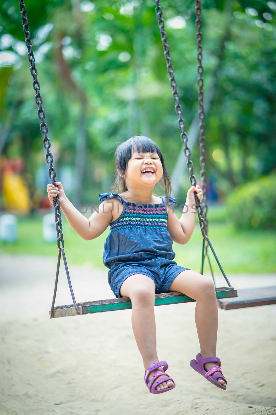 Asian little girl enjoys playing a swing in a children playground