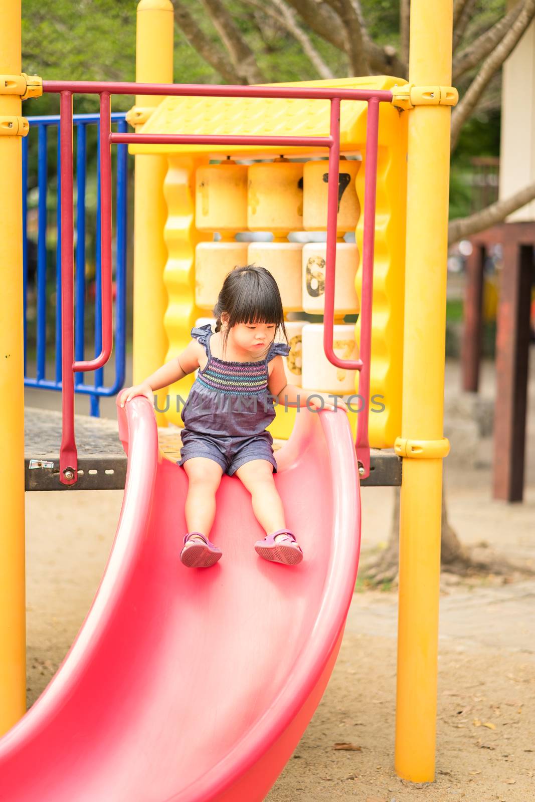 Asian little girl enjoys playing slider in a children playground by domonite