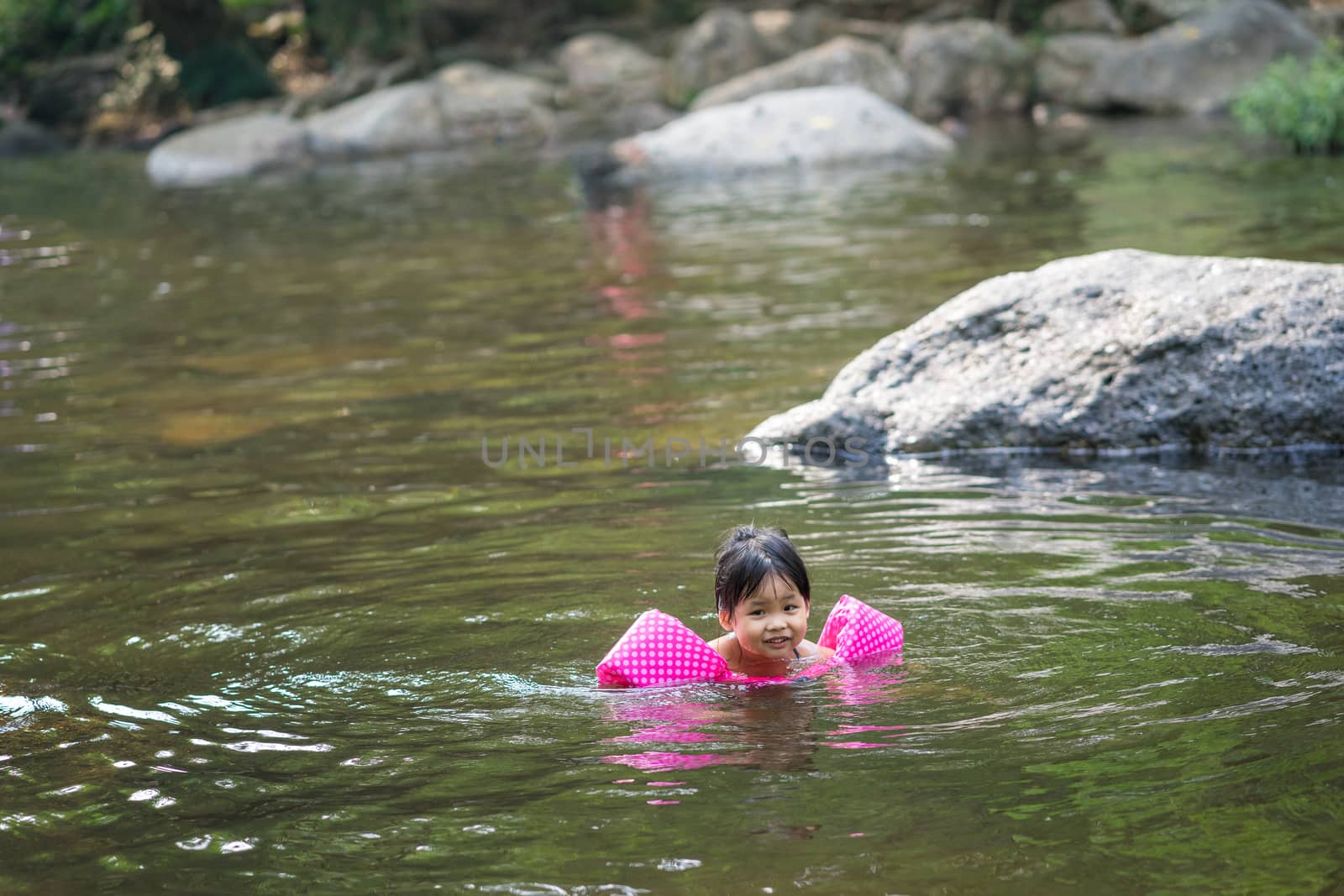 little asian girl wearing inflatable sleeves swimming in nature water on holiday