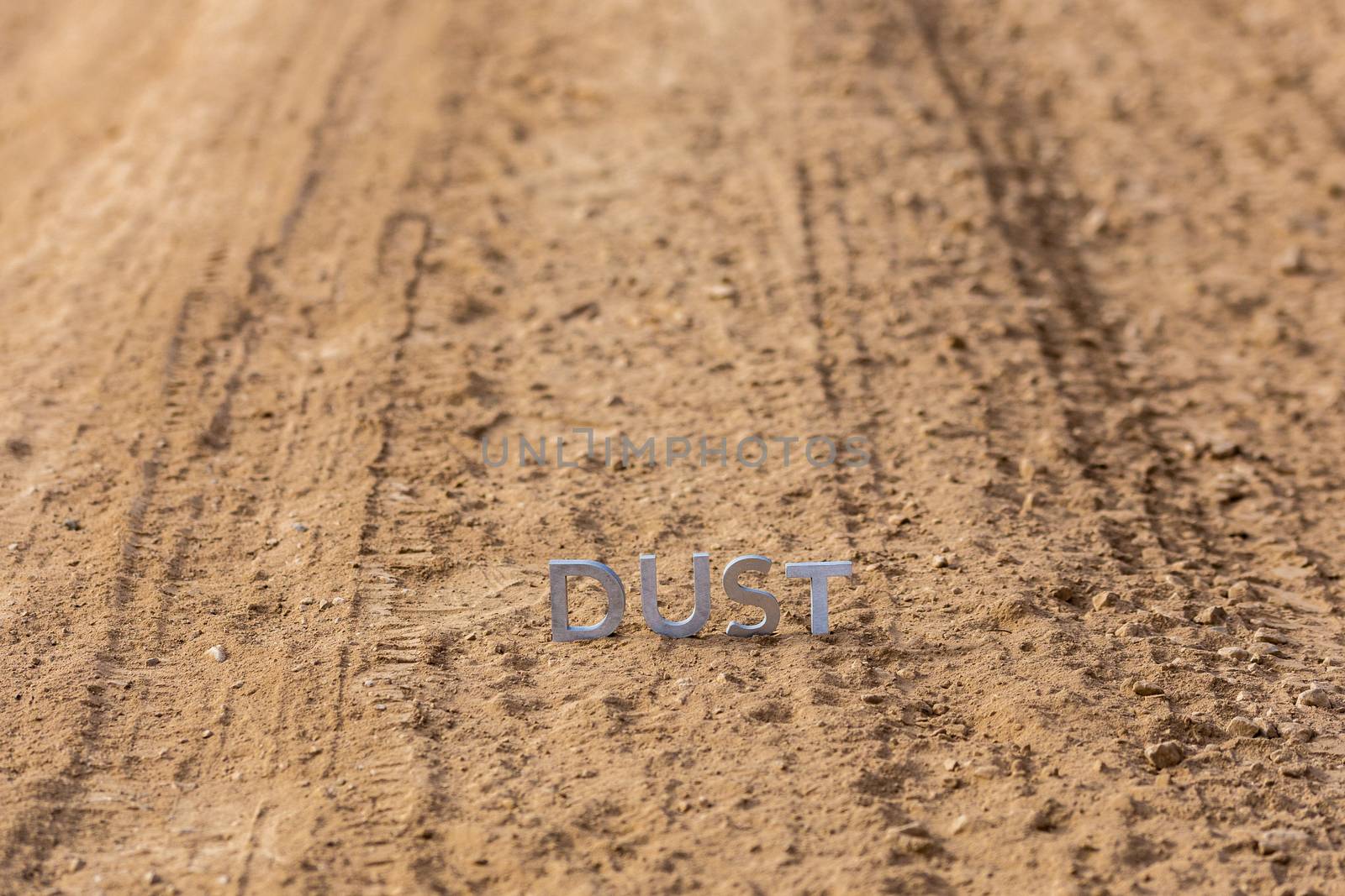 the word dust standing on dusty road surface in linear perspective with selective focus and background blur under direct sunlight