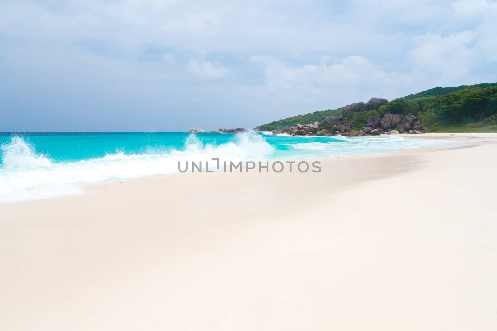White sand beach with some waves and blue sky in the far a hill with green plants