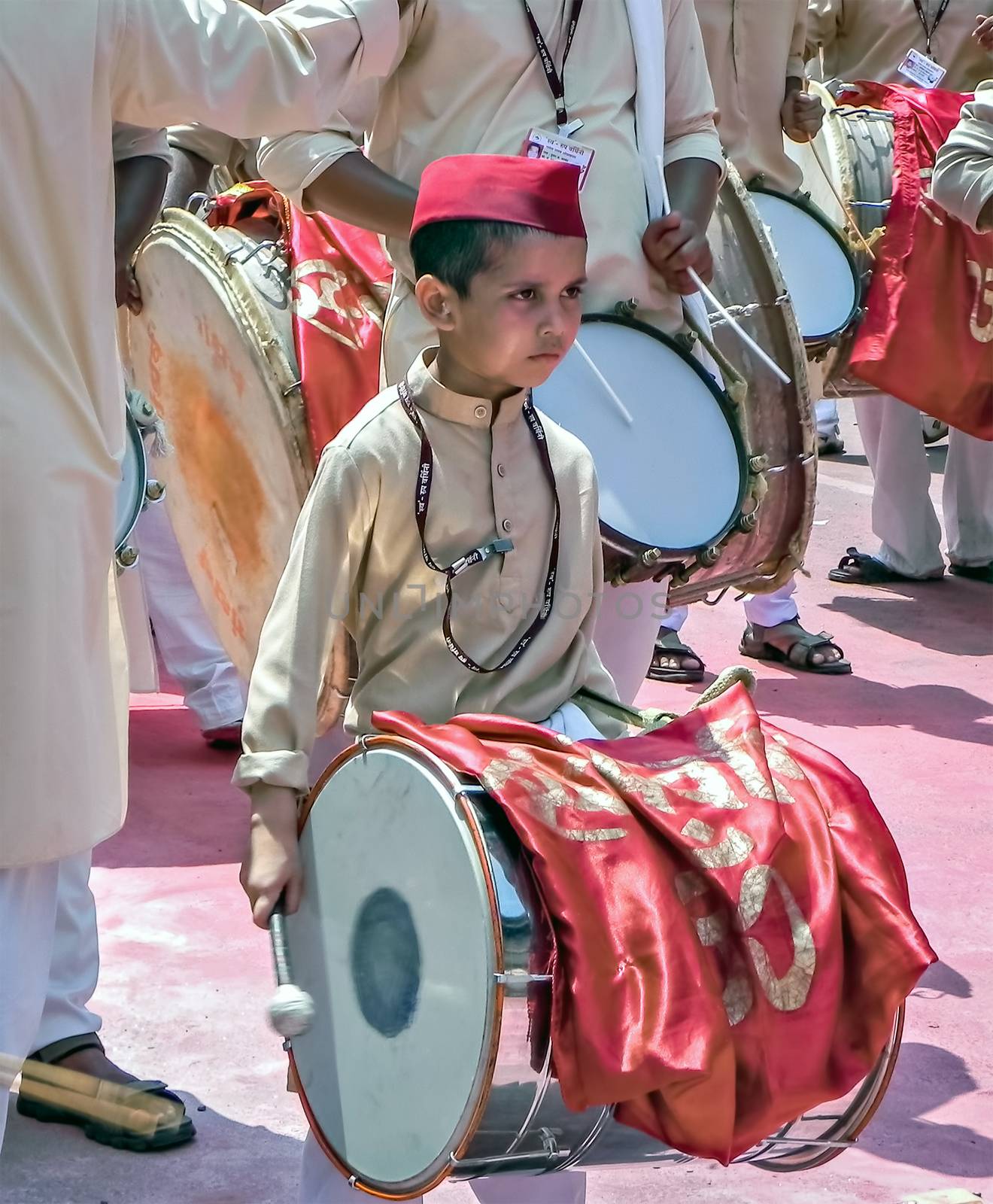 Little boy with red cap beating huge traditional dhol during Ganesh festival. by lalam