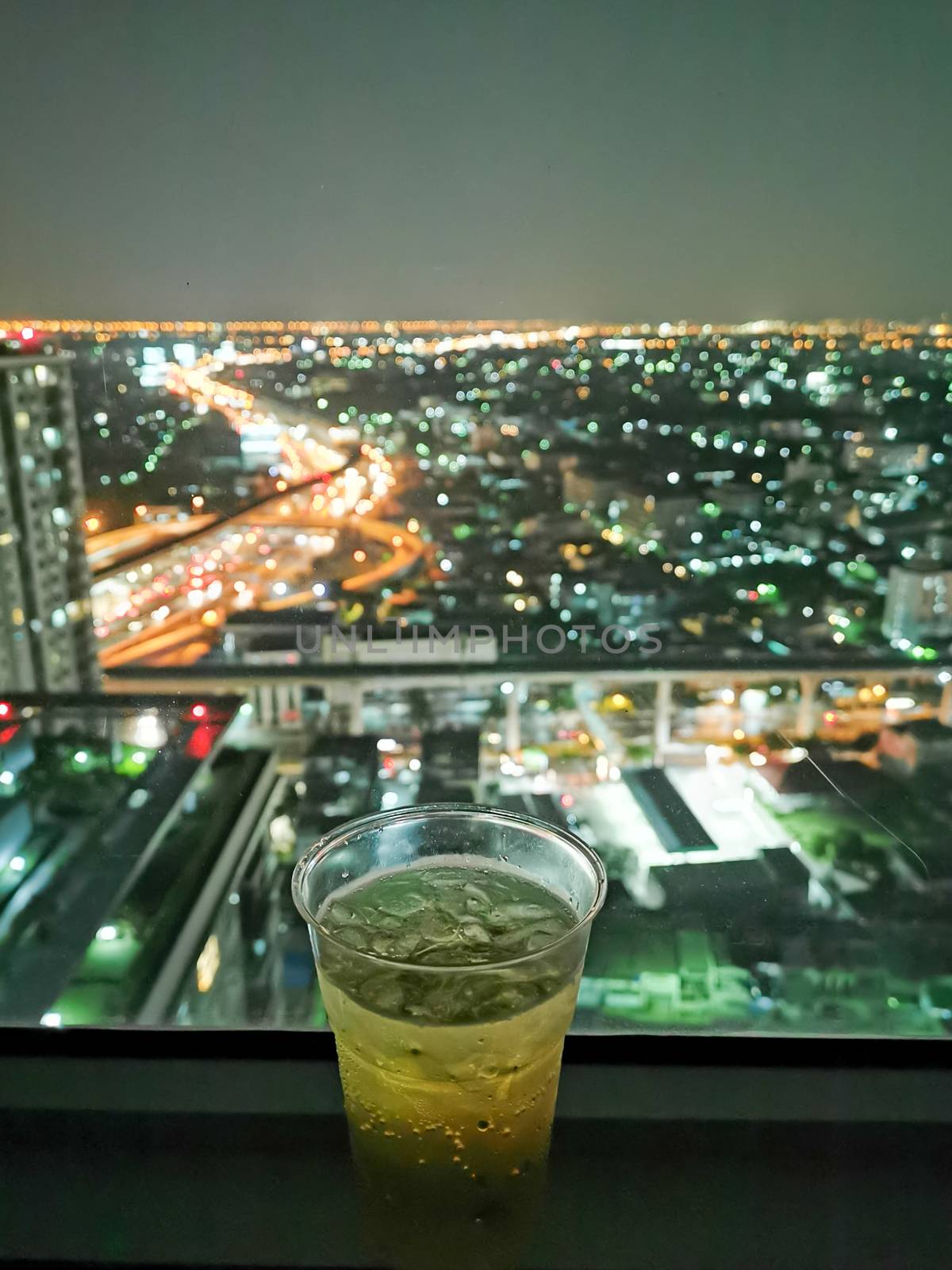 A glass of beer with cityscape from high condominium view at night.
