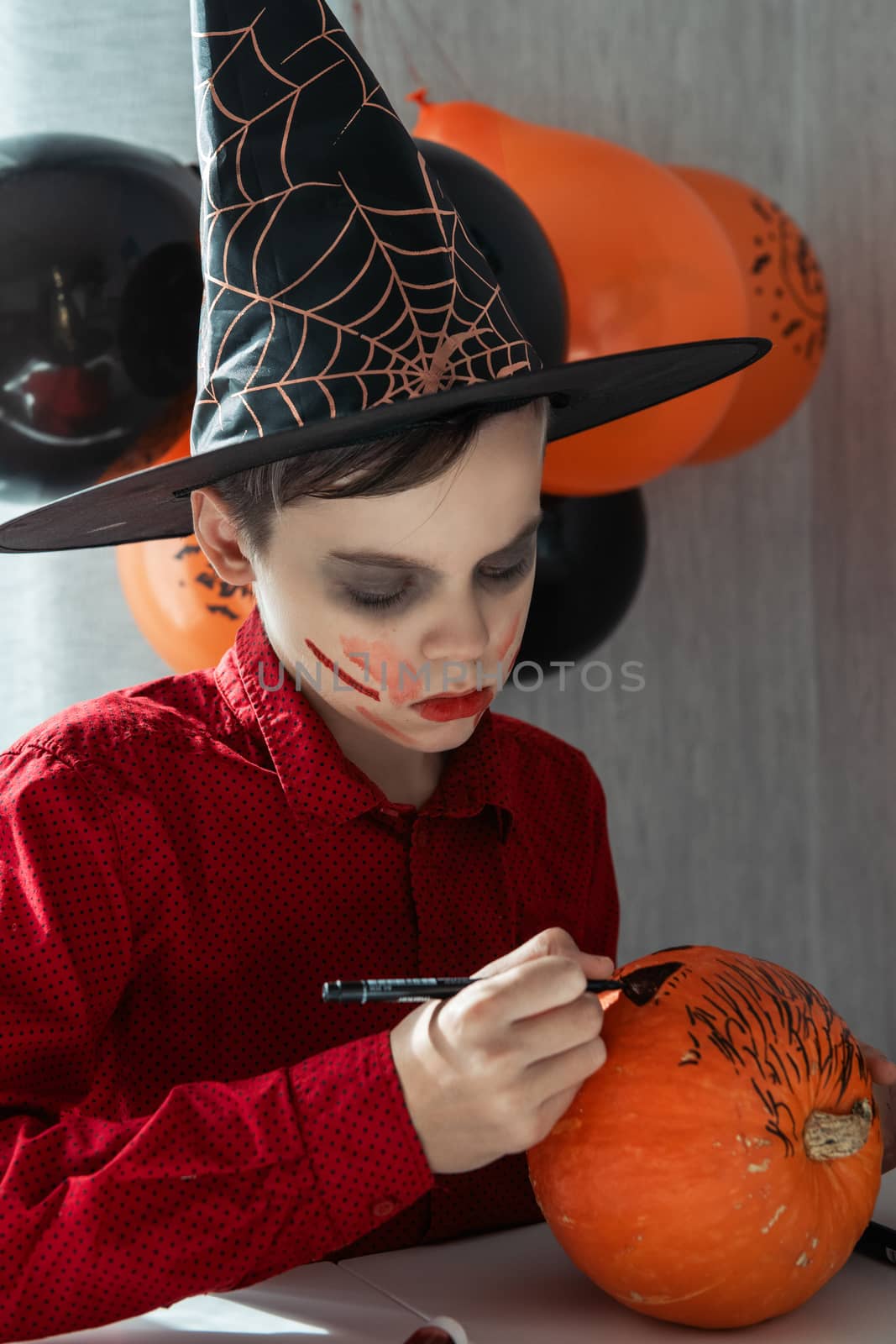 Happy teen boy in costume drawing a pumpkin for the Halloween celebration. by rusak