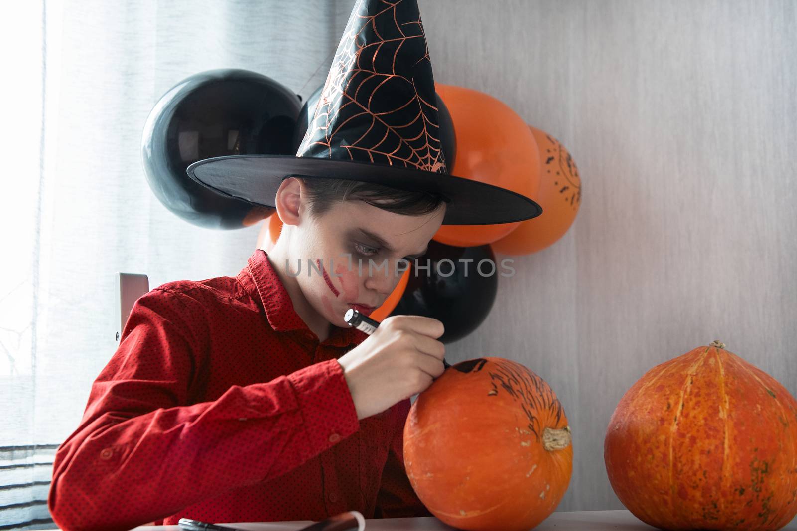 Happy teen boy in costume drawing a pumpkin for the Halloween celebration. by rusak