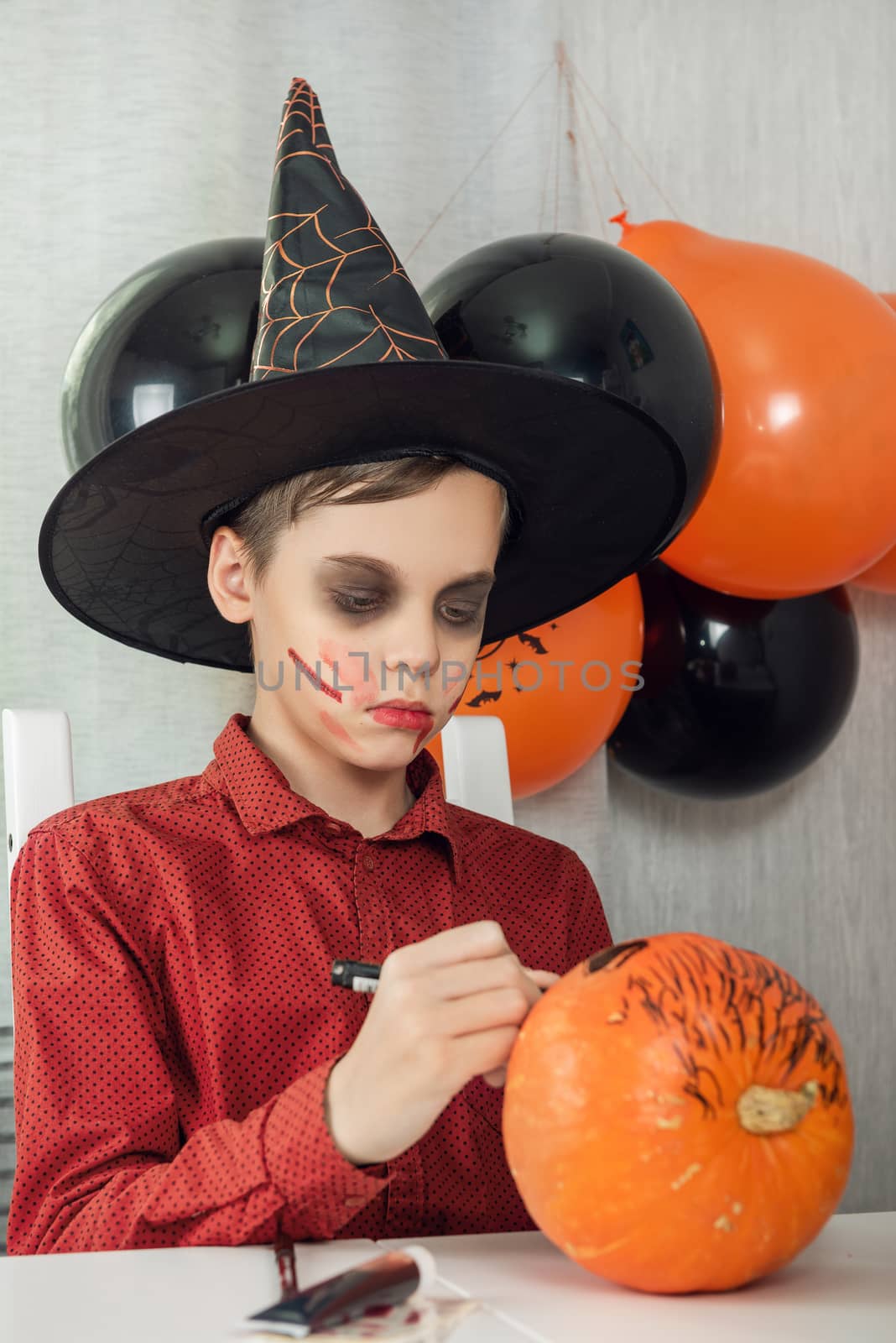 Happy teen boy in costume drawing a pumpkin for the Halloween celebration. by rusak