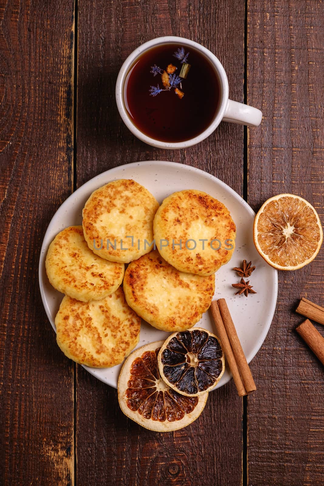 Cottage cheese fritters with hot black aromatic tea, Christmas breakfast mood with anise, cinnamon and dried citrus on wooden background, top view
