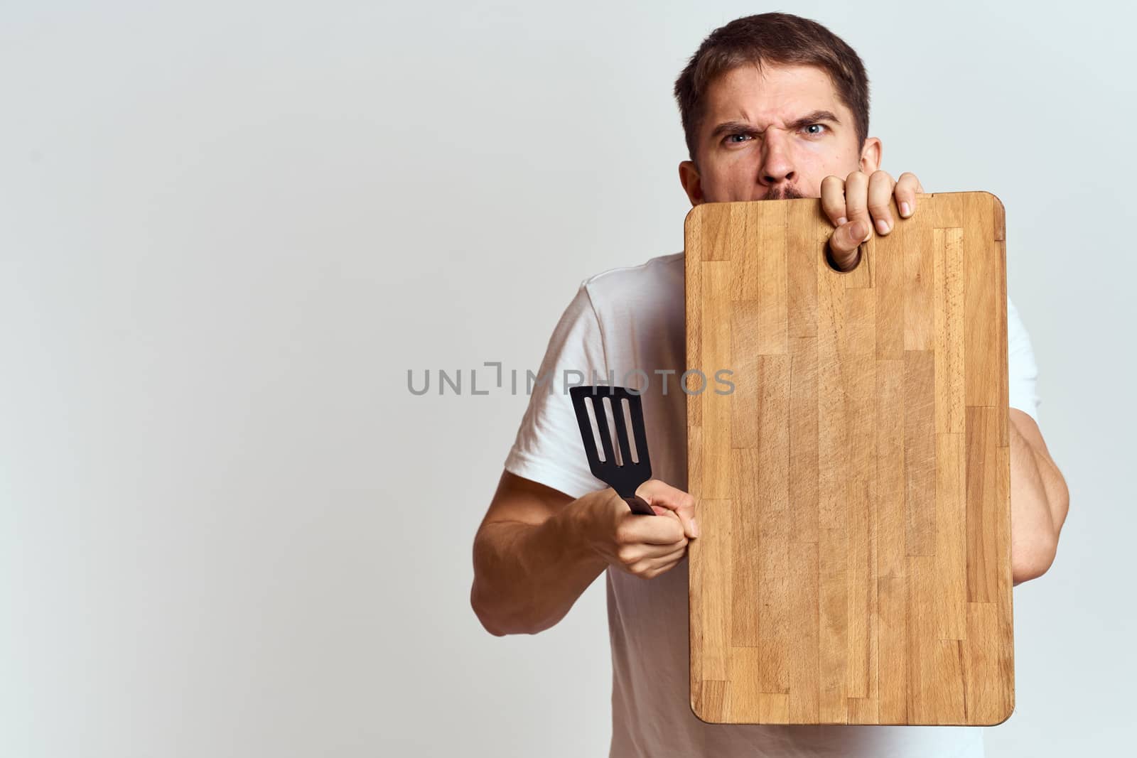 Man with a kitchen wooden board and with a shovel on a light background emotions white t-shirt model by SHOTPRIME