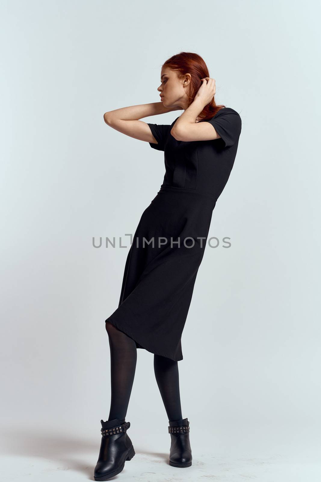 A woman in a black dress on a light background and pantyhose shoes red hair and pose in full growth by SHOTPRIME