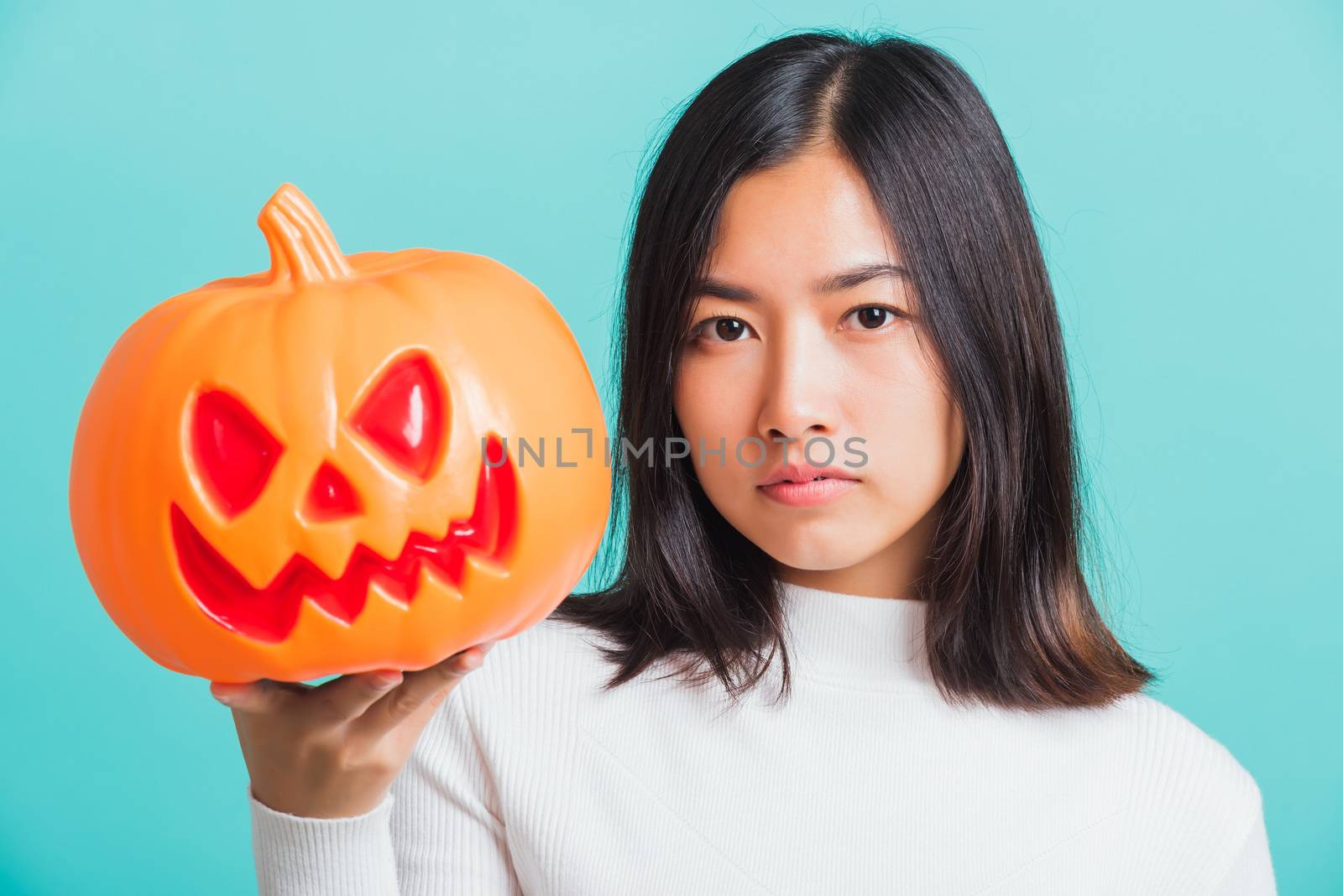 Portrait of Asian beautiful young woman holding orange model pumpkins, funny happy female with ghost pumpkins, studio shot isolated on blue background