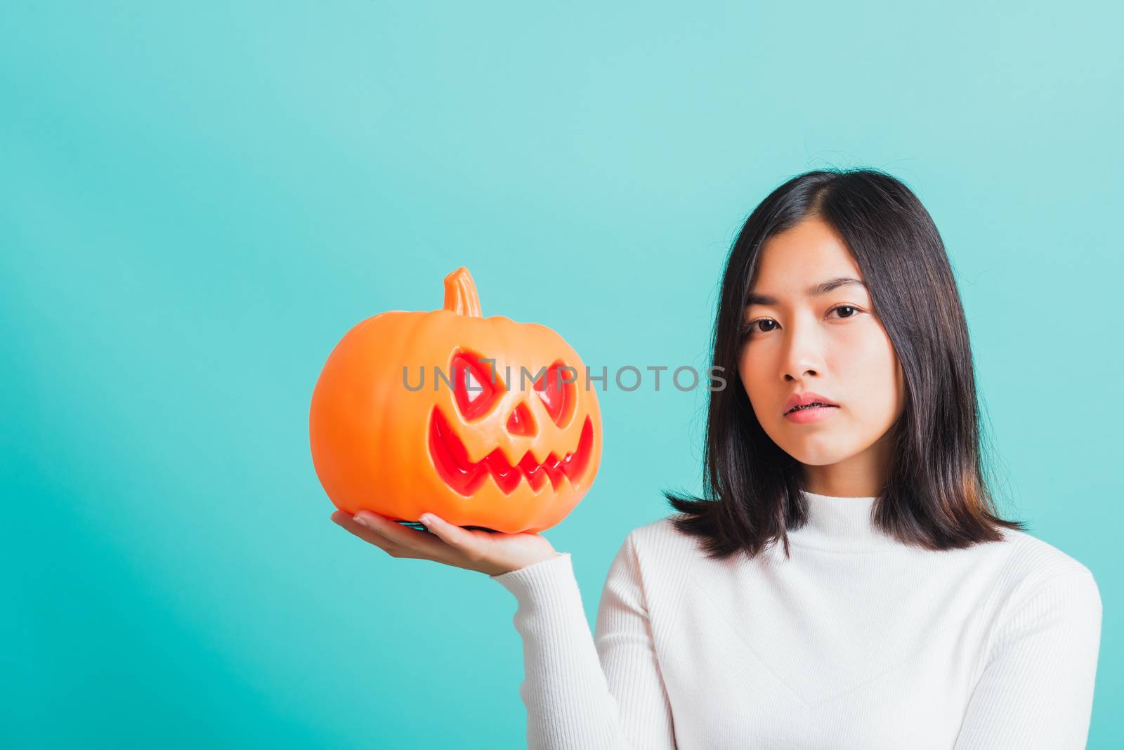 Portrait of Asian beautiful young woman holding orange model pumpkins, funny happy female with ghost pumpkins, studio shot isolated on blue background