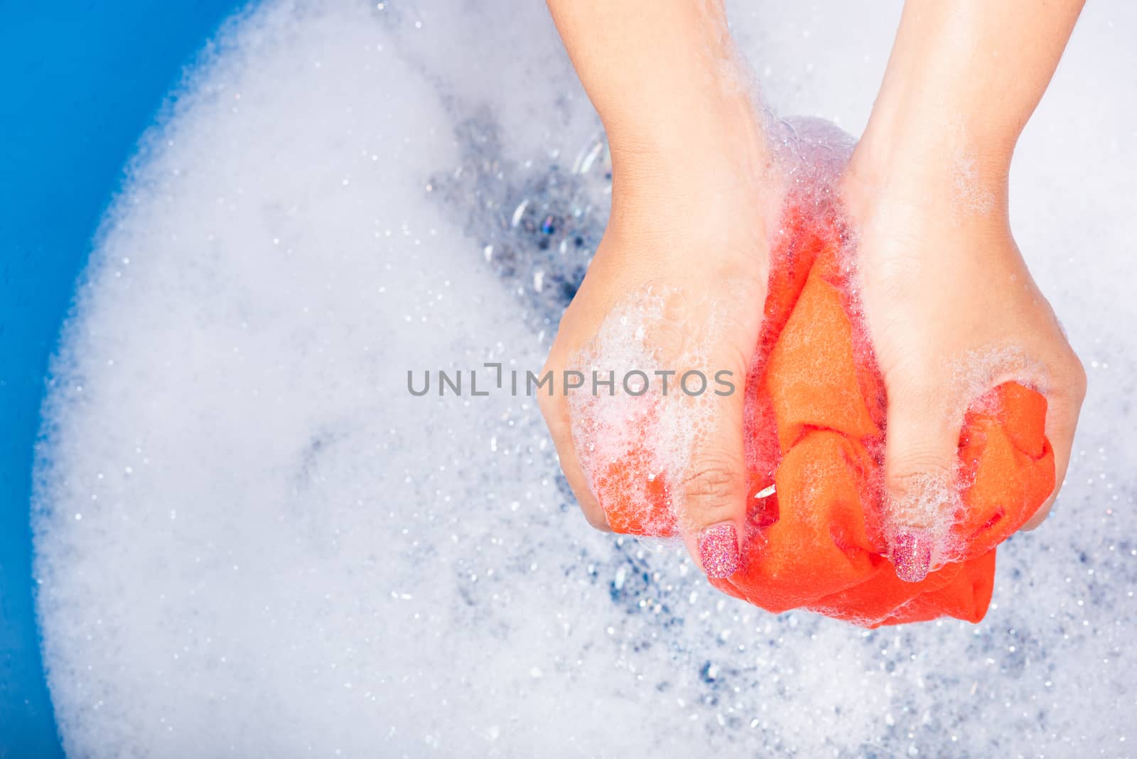 Closeup young Asian woman use hands washing color clothes in basin with detergent have soapy bubble water, studio shot background, laundry concept