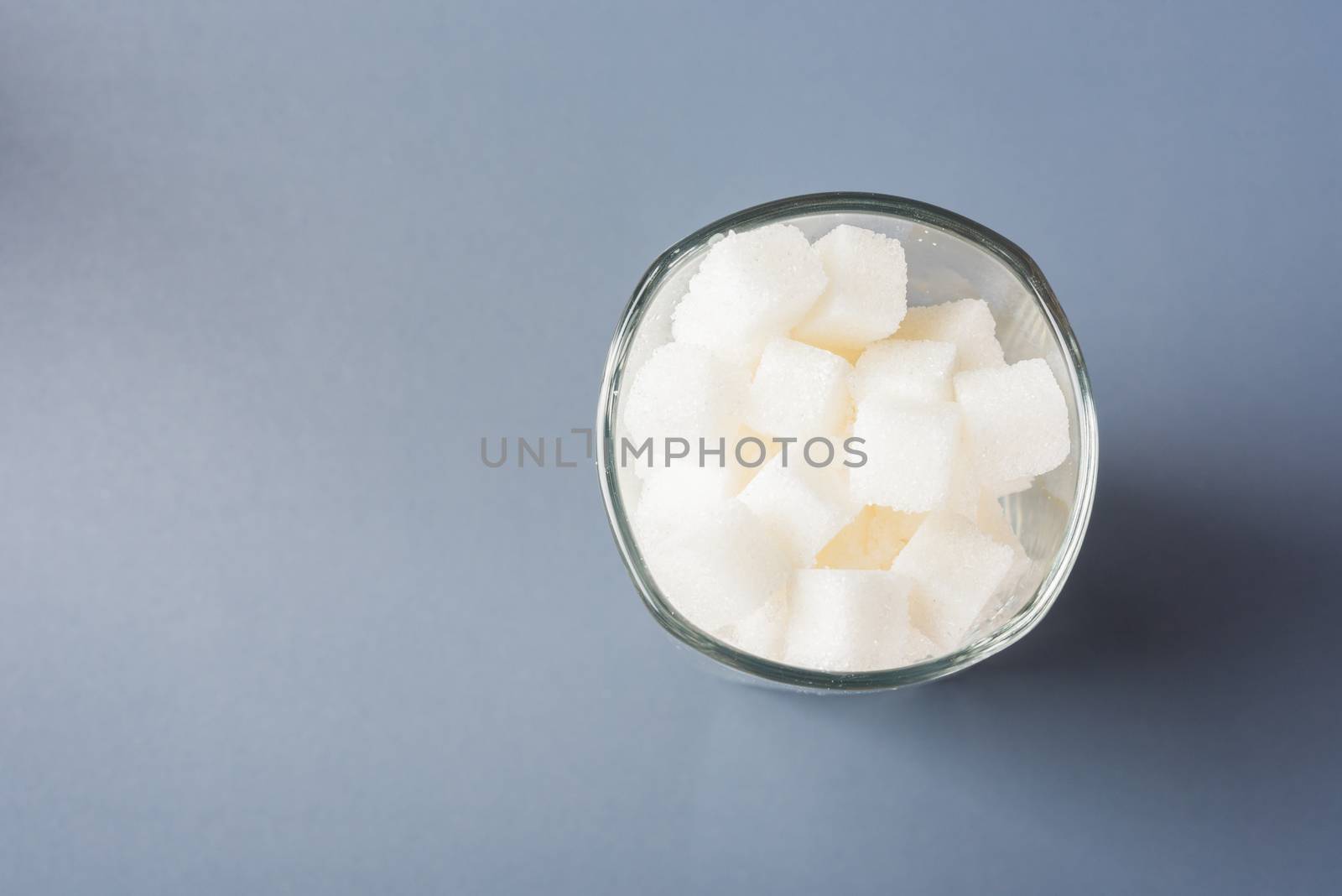 Top view glass full of white sugar cube sweet food ingredient, studio shot isolated on gray background, health high blood risk of diabetes and calorie intake concept and unhealthy drink