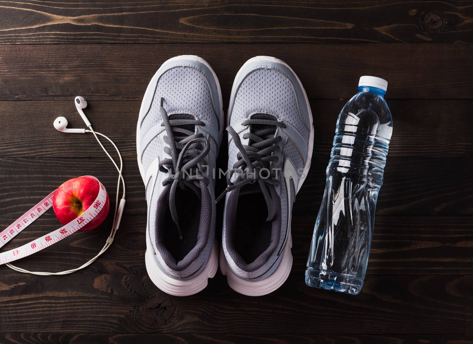Pair sports shoes, headphones, apple and water bottle on black w by Sorapop