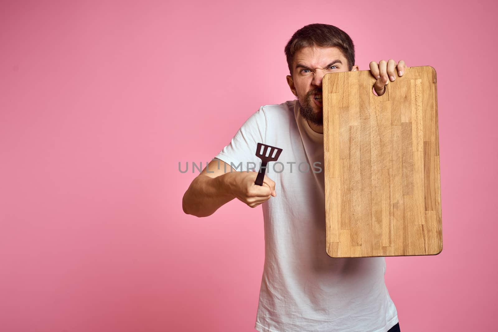 guy holding kitchen board and spatula in hand on pink background cropped view by SHOTPRIME