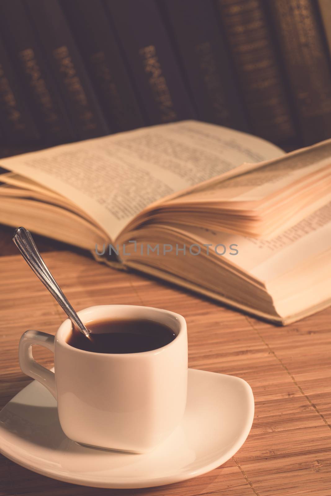An open book and a cup of coffee on the table. Reading a book in a cafe. Stylish photo of the coffee house. A cup of coffee in the evening light.