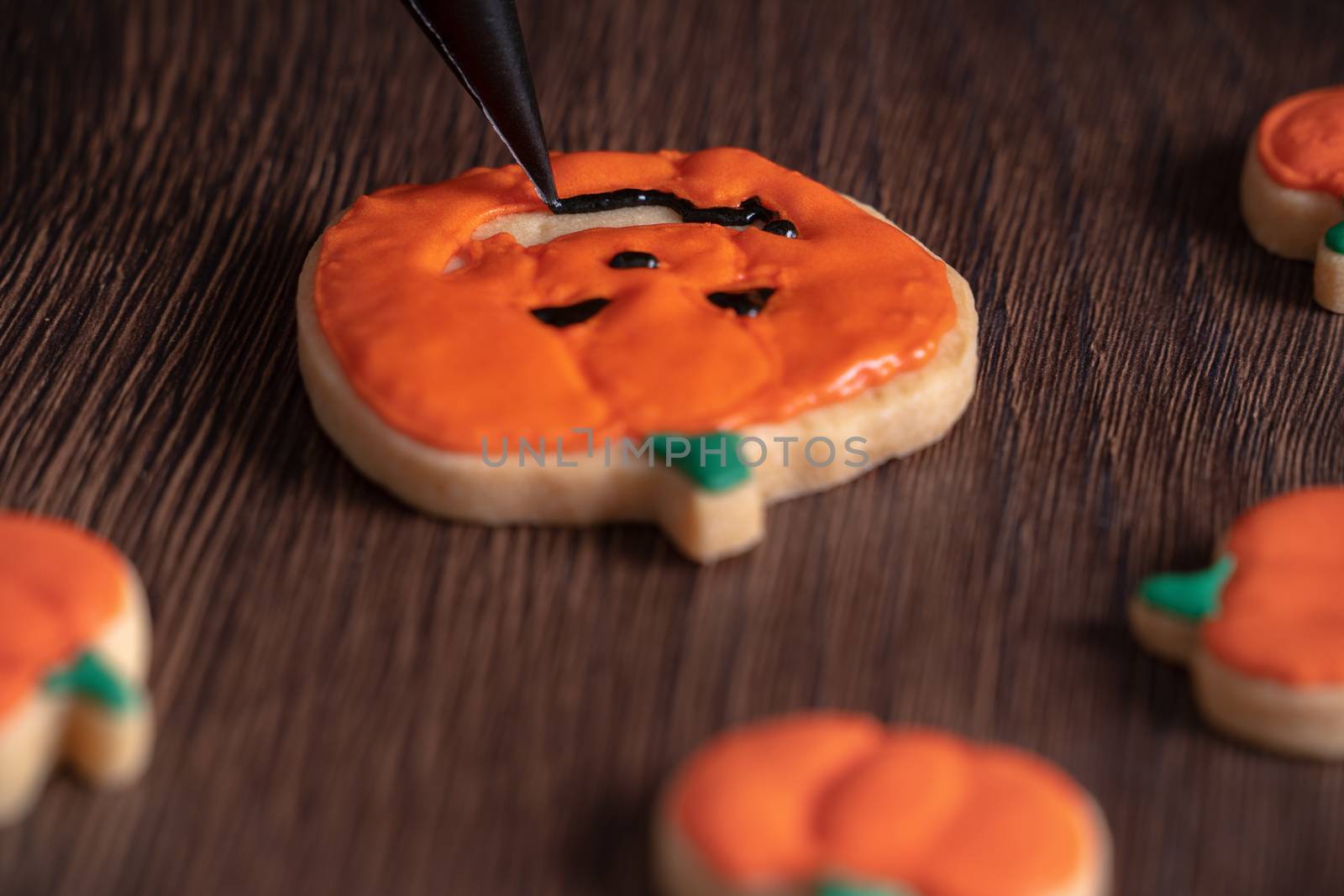 Close up of decorating cute Halloween pumpkin gingerbread cookies with frosting icing cream topping bag.
