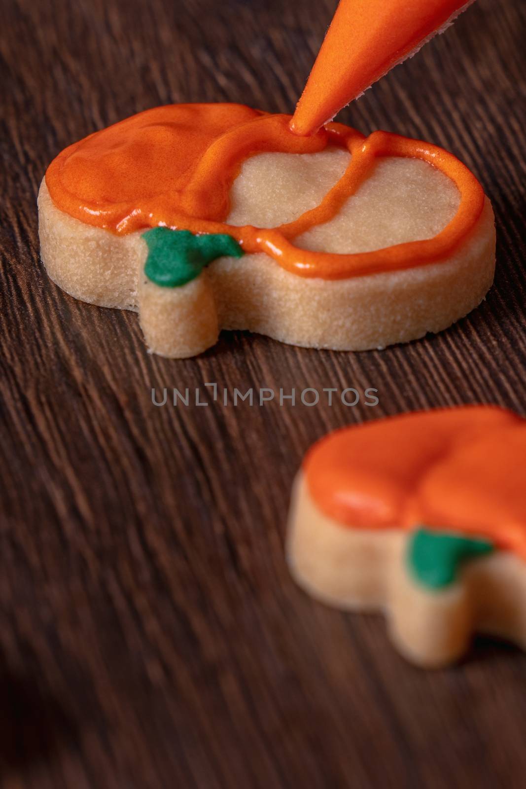 Close up of decorating cute Halloween pumpkin gingerbread cookies with frosting icing cream topping bag.