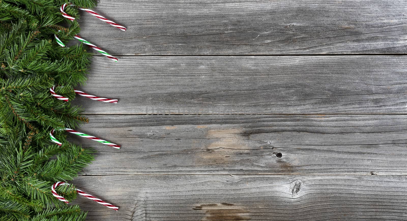 Merry Christmas and Happy New Year holiday concept with candy cane decorations on left side of weathered wooden boards
