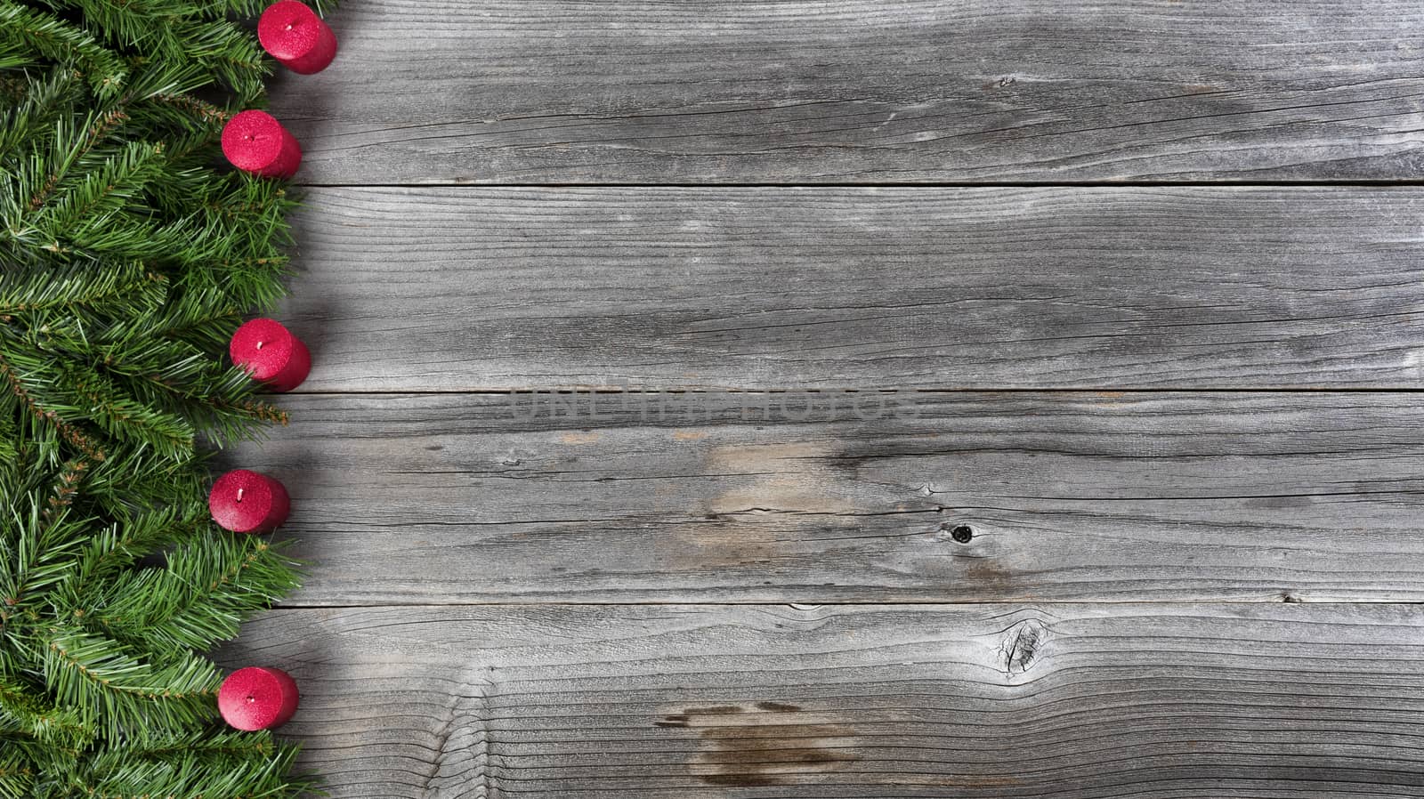 Merry Christmas and Happy New Year concept consisting of fir branches and red candles on left side of rustic wooden boards