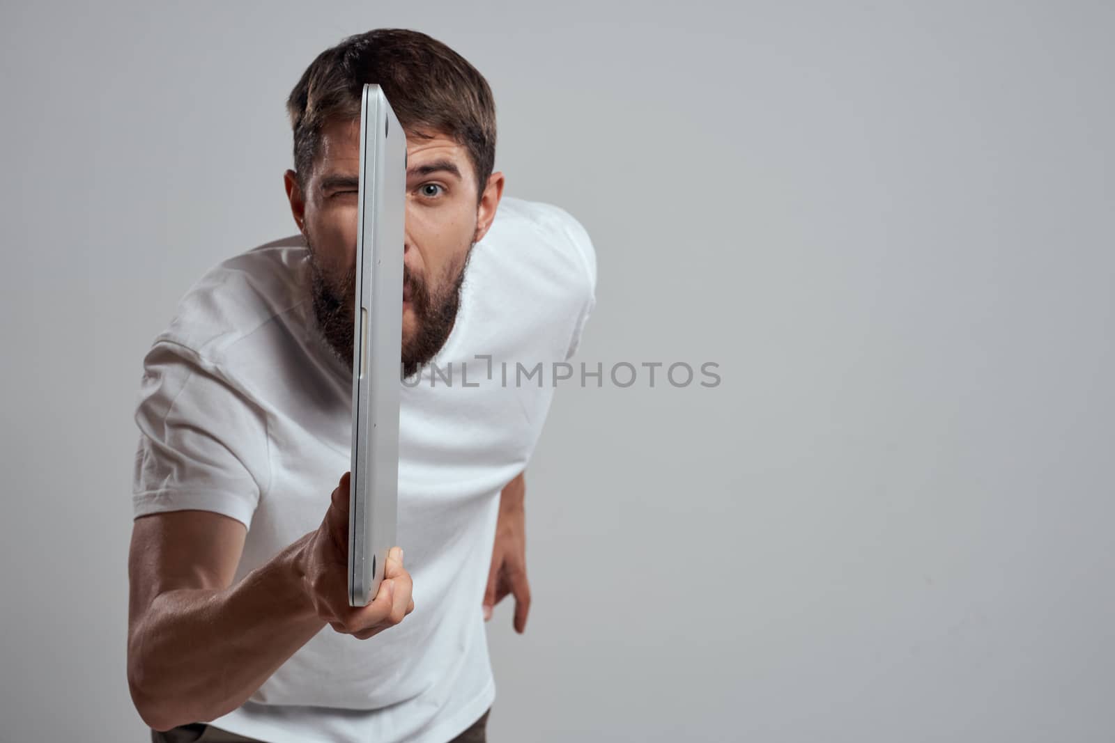 A man with a laptop in his hands on a light background in a white t-shirt emotions light background cropped view model portrait new technologies. High quality photo