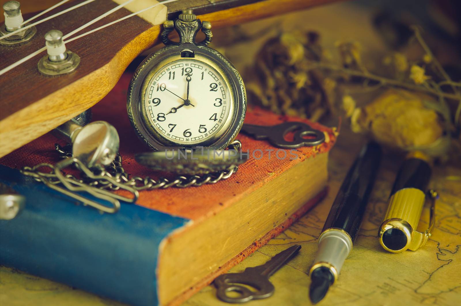 An antique pocket watch leaned against a ukulele and old book. by SaitanSainam