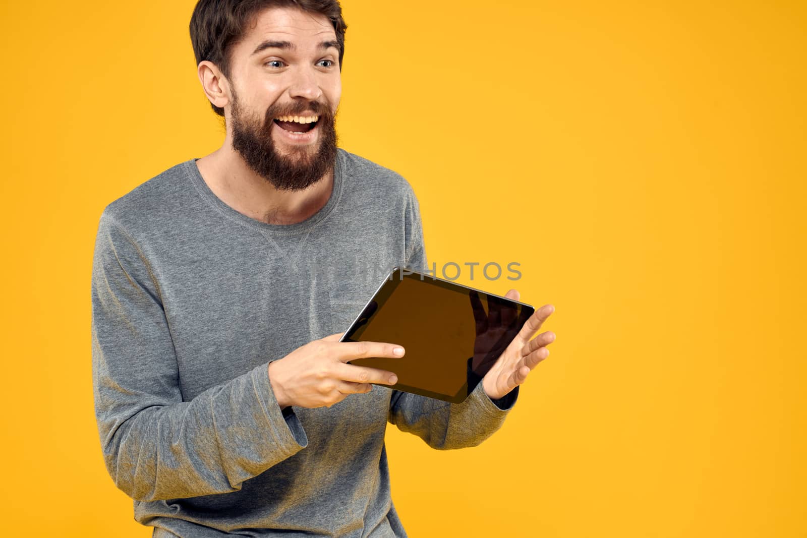 Emotional man with tablet in hands technology internet device lifestyle yellow background. High quality photo