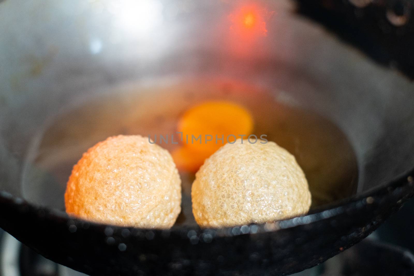 shot of north indian street food snack gol gappe pani puri or puchke being fried from dough in hot oil to make them round hollow golden ball spheres by Shalinimathur