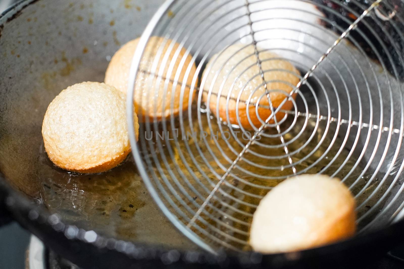 shot of north indian street food snack gol gappe pani puri or puchke being fried from dough in hot oil to make them round hollow golden ball spheres. Shows the preparation of one of the favorite snacks of India being made in a home kitchen or a small business owners home for selling as street food