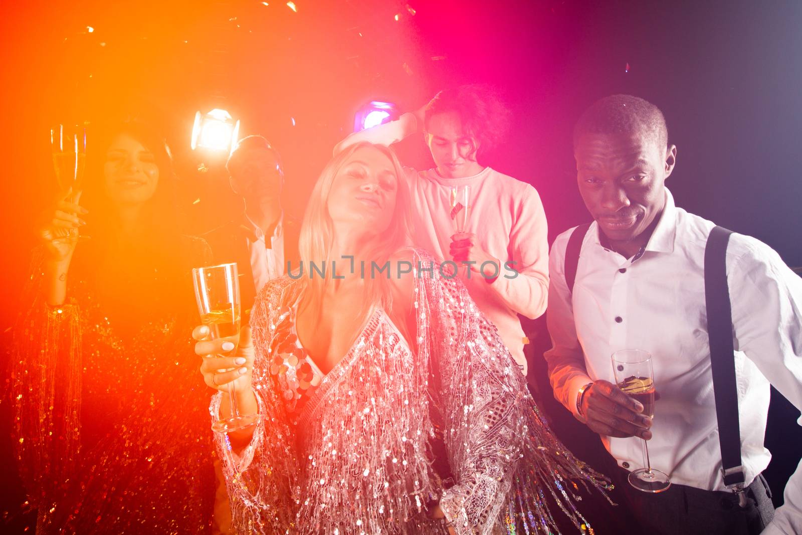 People having fun at 80s retro style party. People wearing costumes drinking champagne and dancing on dancefloor at nightclub in golden confetti