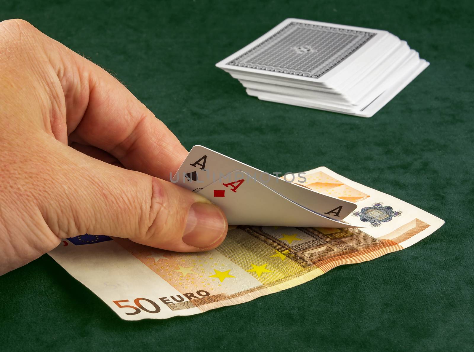 
On the table lay banknote, and a man's hand lifts two cards at poker game