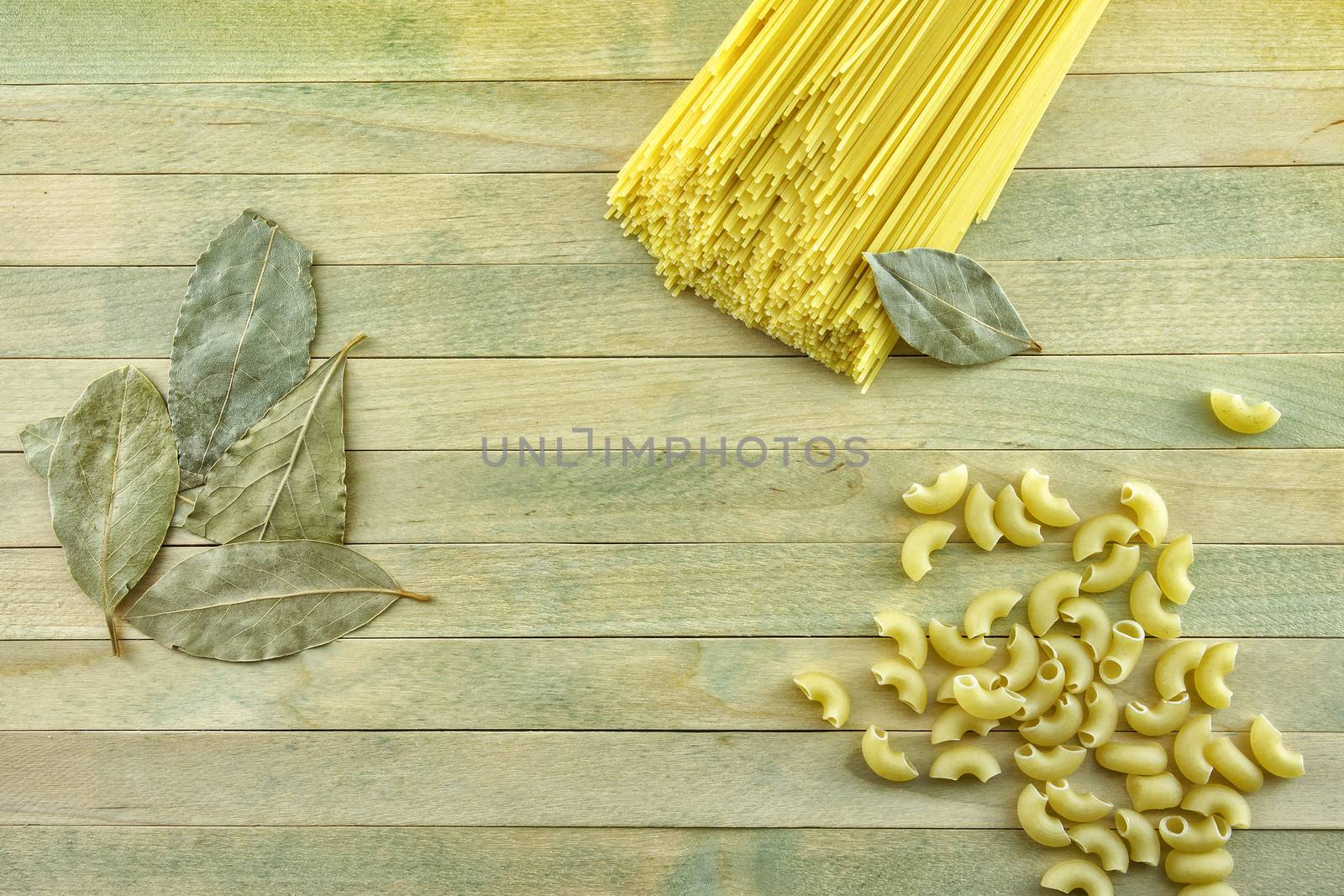 On a wooden surface lie bay leaves and pasta