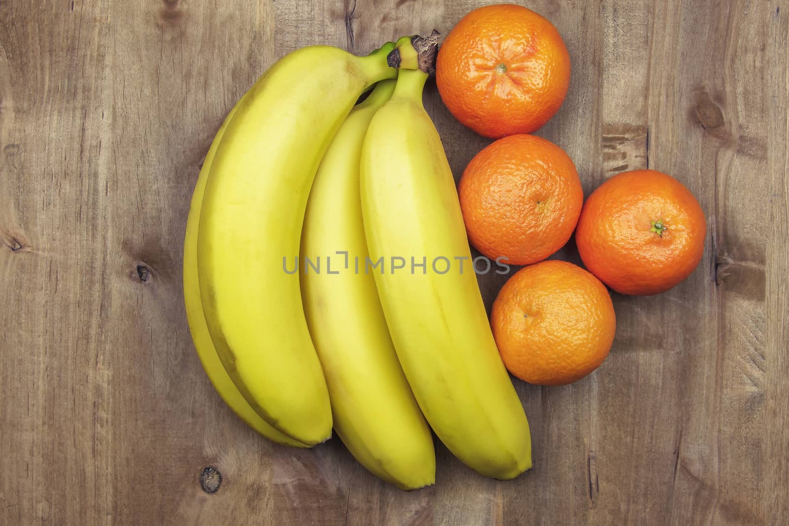 Bunch of bananas and tangerines lie on a wooden surface by Grommik