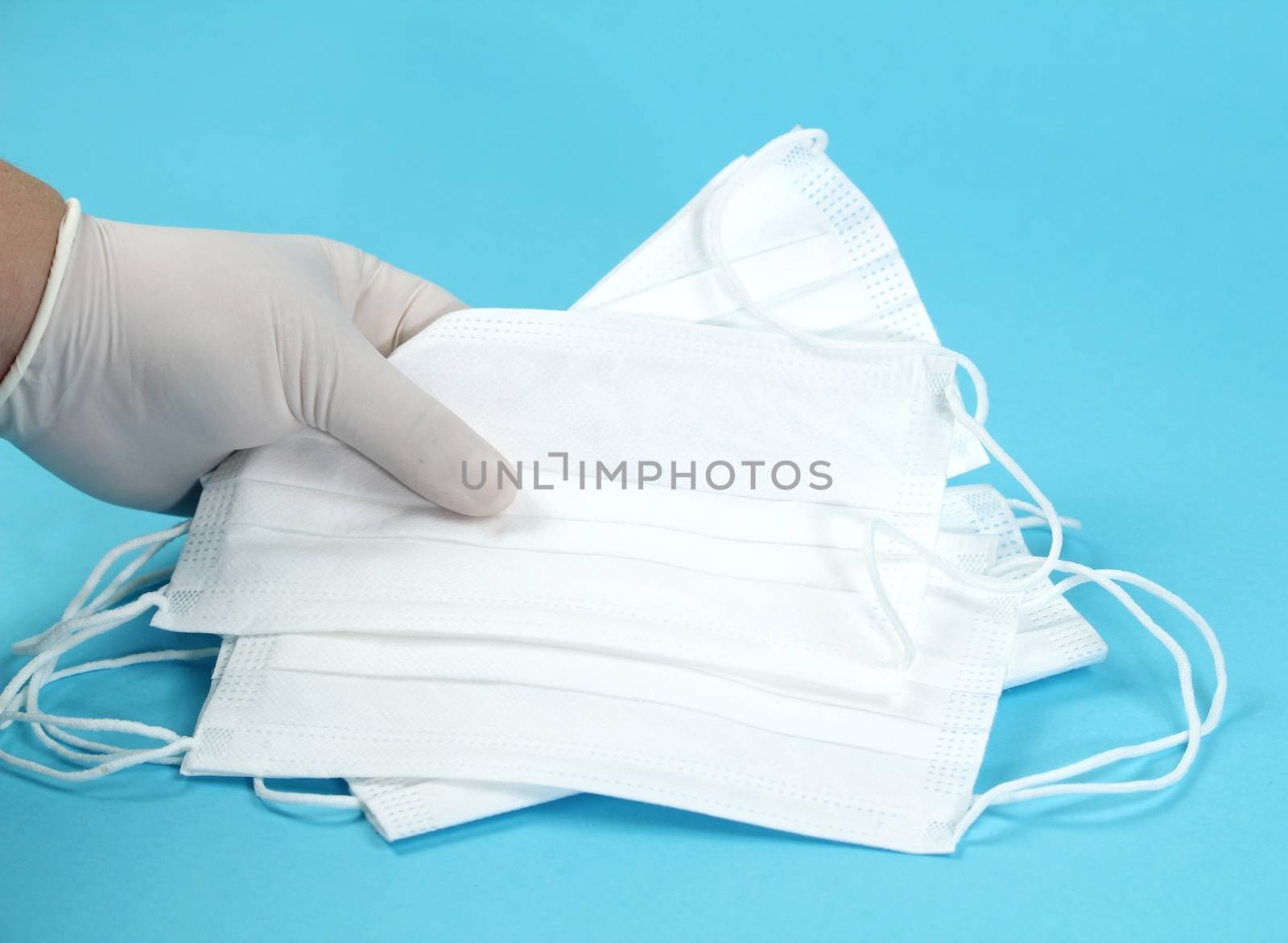 Hand with surgical gloves hanging Disposable Medical masks on blue background. Covid-19 and healthcare concept