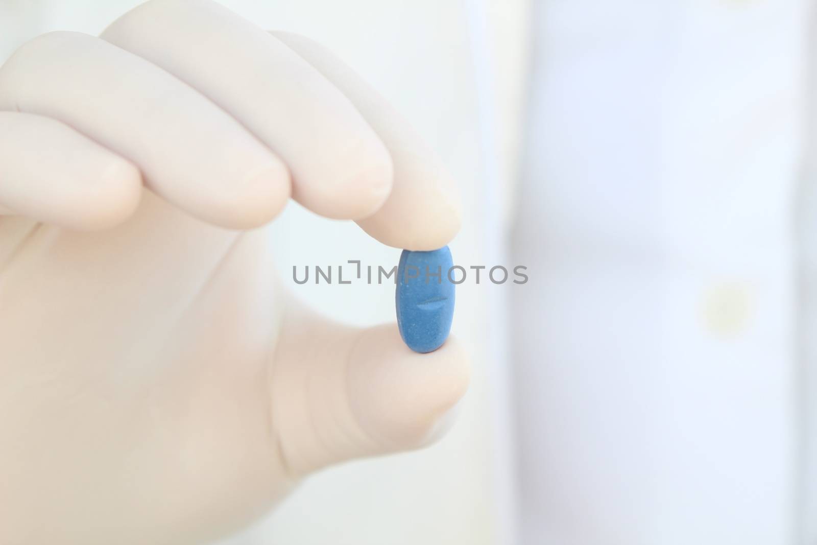 Male hand in white surgical glove holding a pill