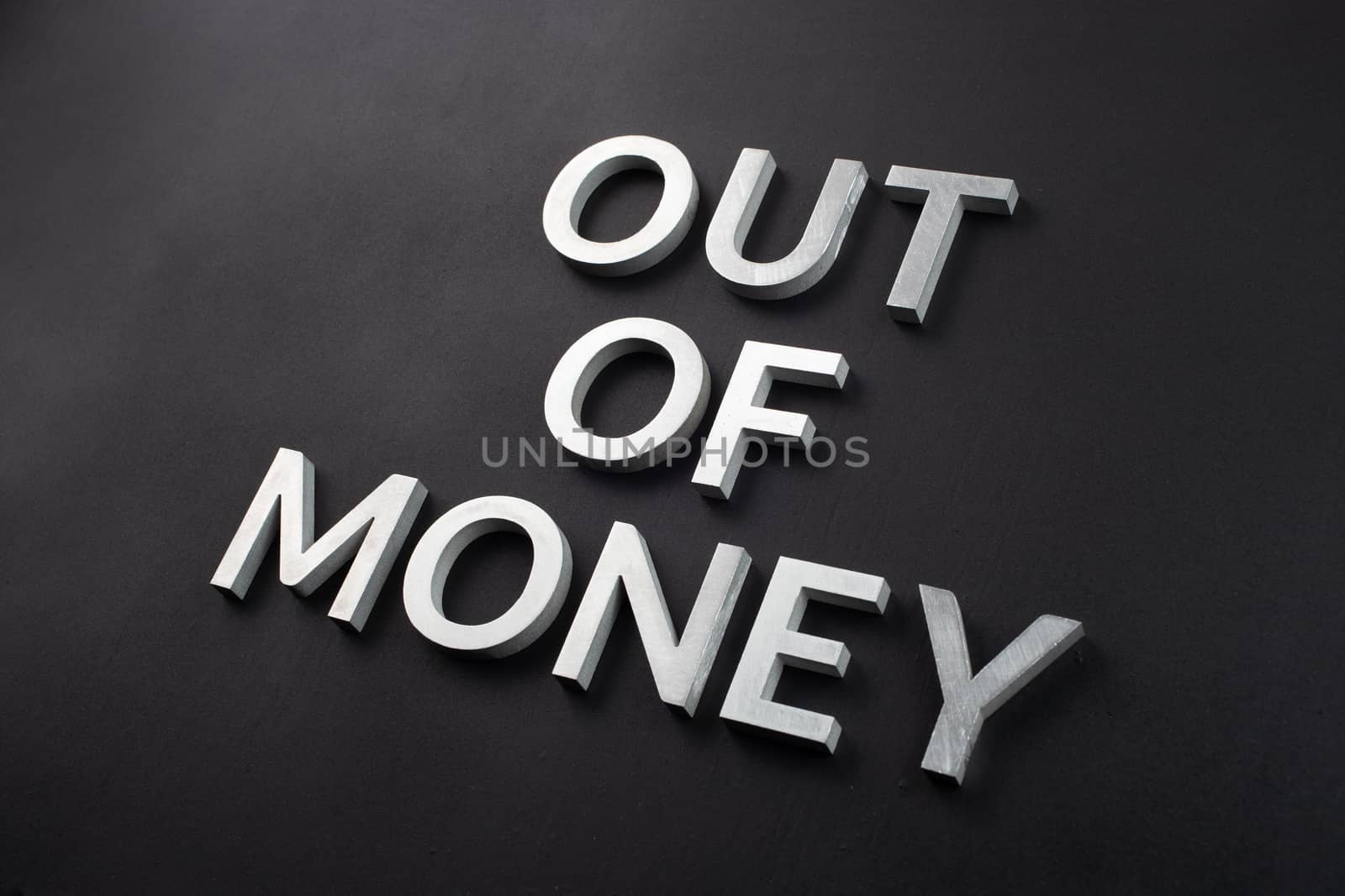 the words out of money laid with white brushed metal letters on flat matte black surface in diagonal perspective with selective focus