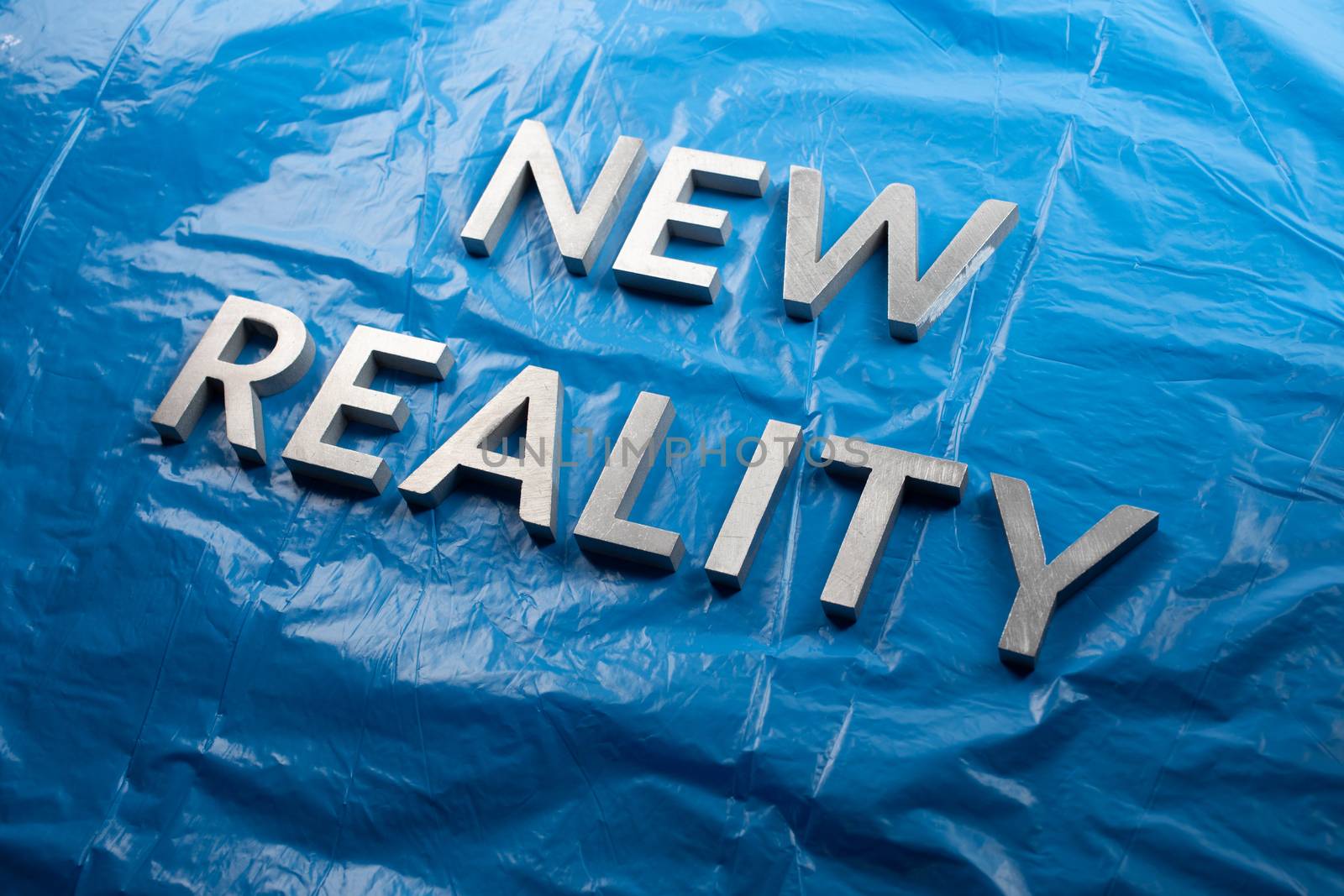 the words new reality laid with white letters over crumpled blue plastic film background in slanted perspective