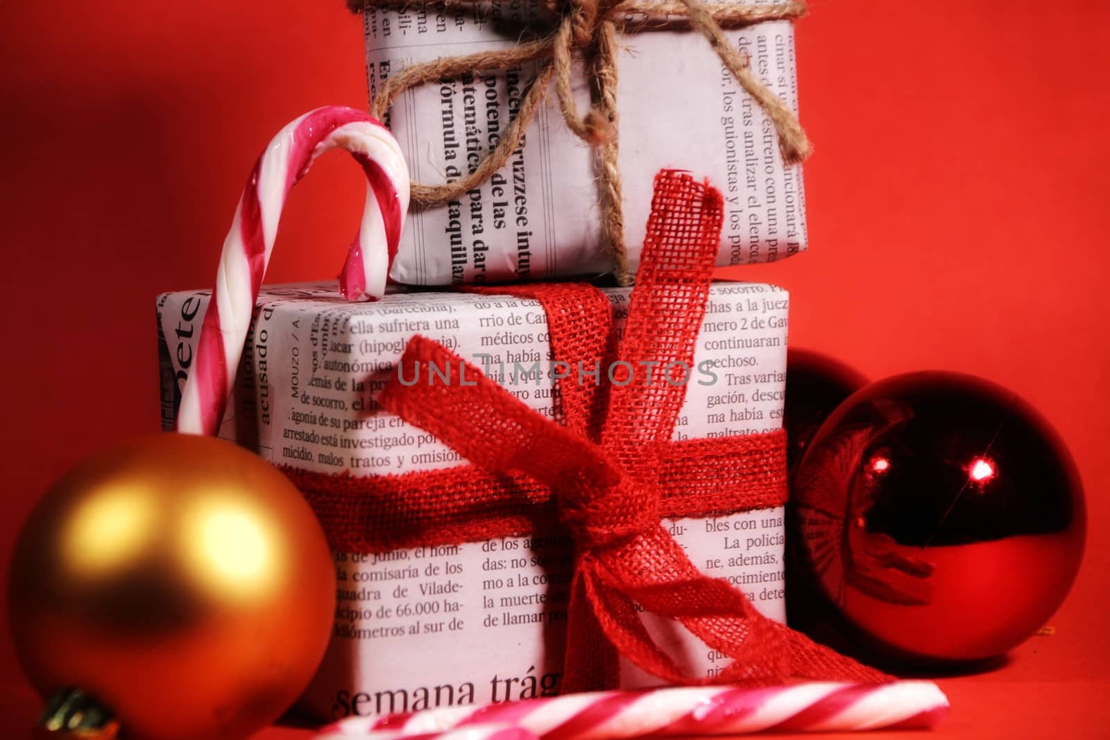 Gifts wrapped in old newspaper with red bow and rope on red background