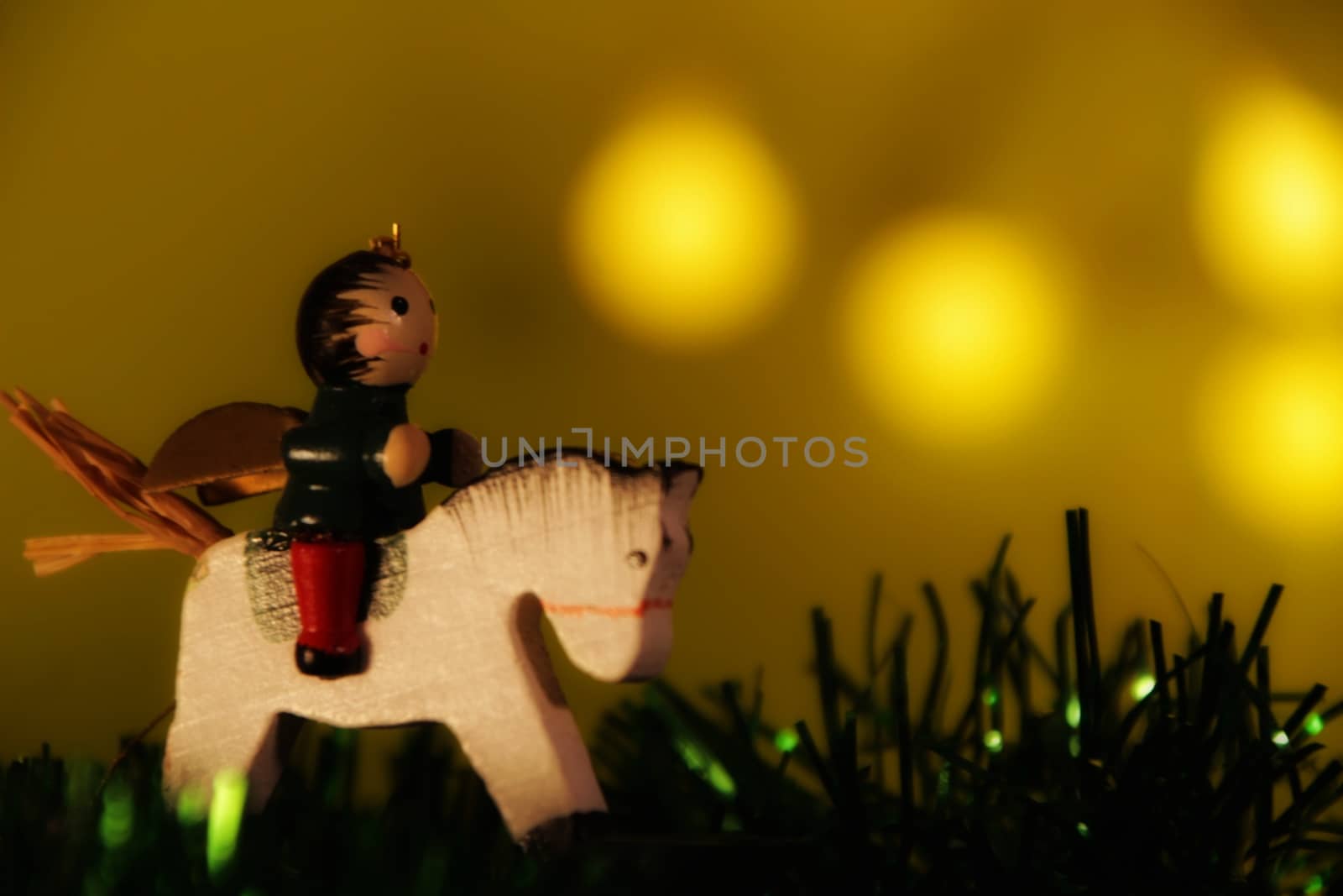 Beautiful Angel Christmas ornament ridding a horse with green garland. Light Green with lights background 