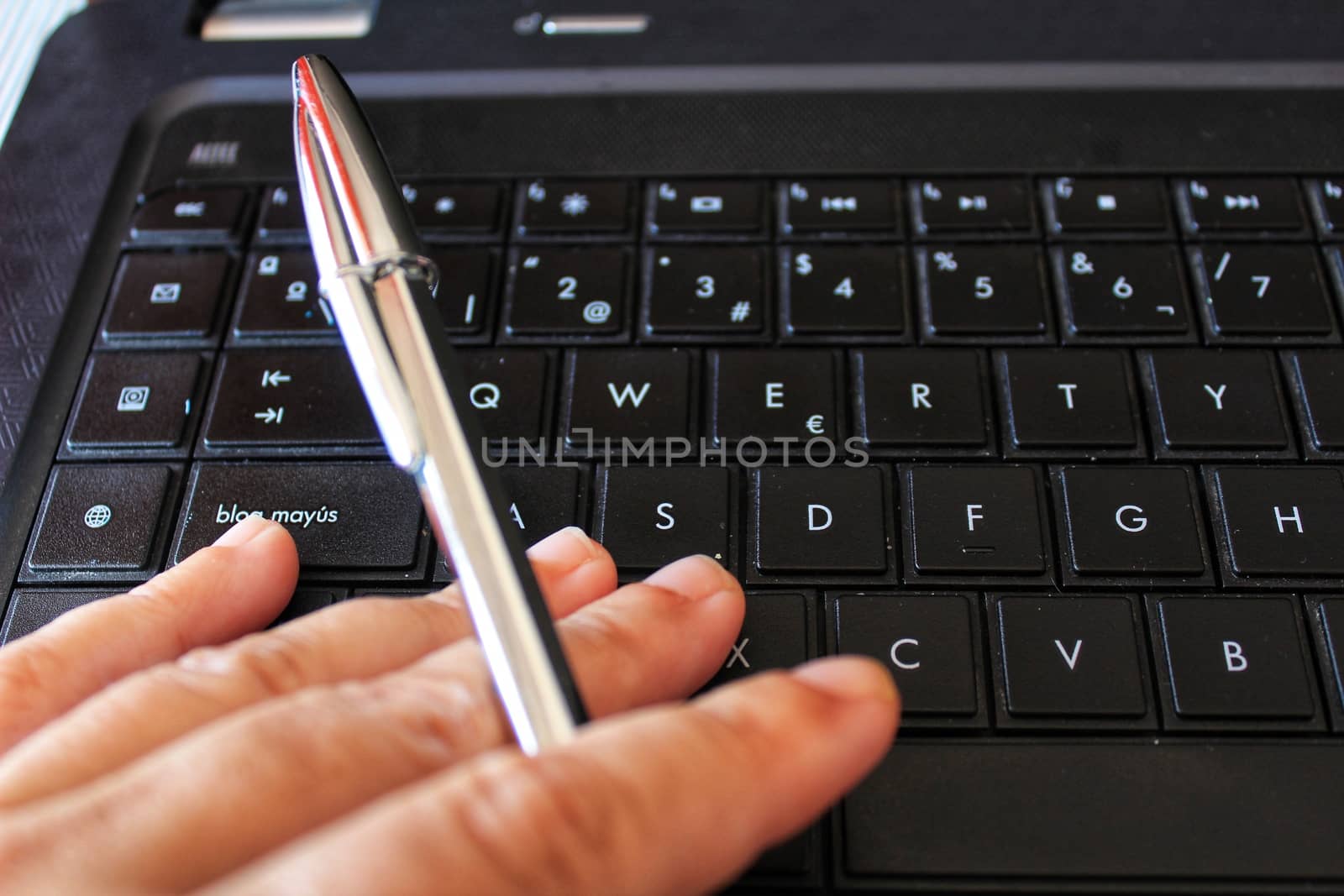 Hand with pen on black keyboard laptop while working