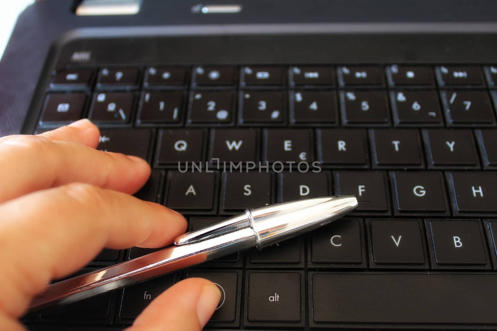 Hand with pen on black keyboard laptop by soniabonet