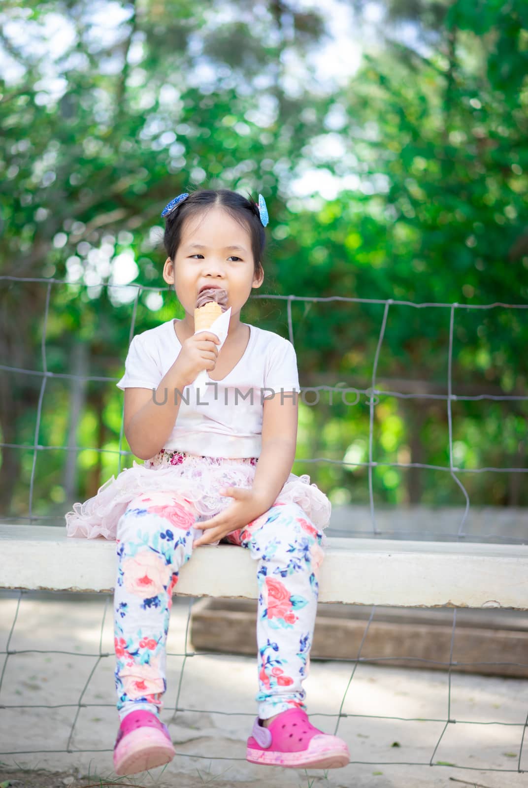 Asian little girl eating an ice cream outdoors with natural light blur background