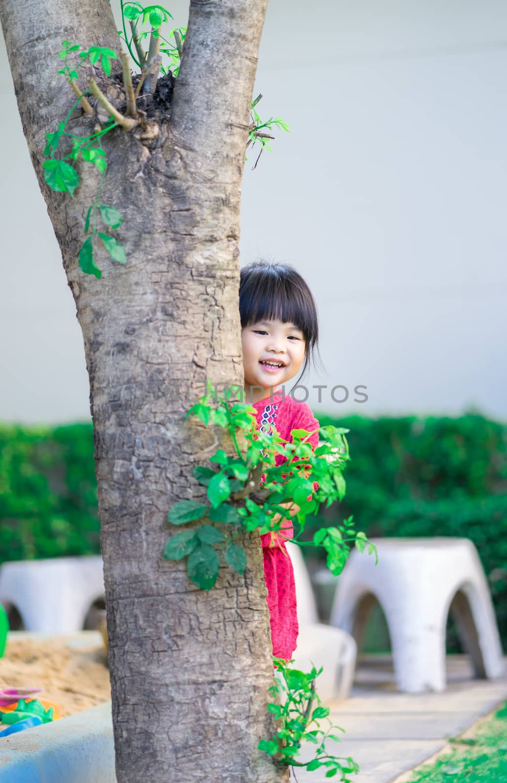 little girl sneaking behind the tree in the park